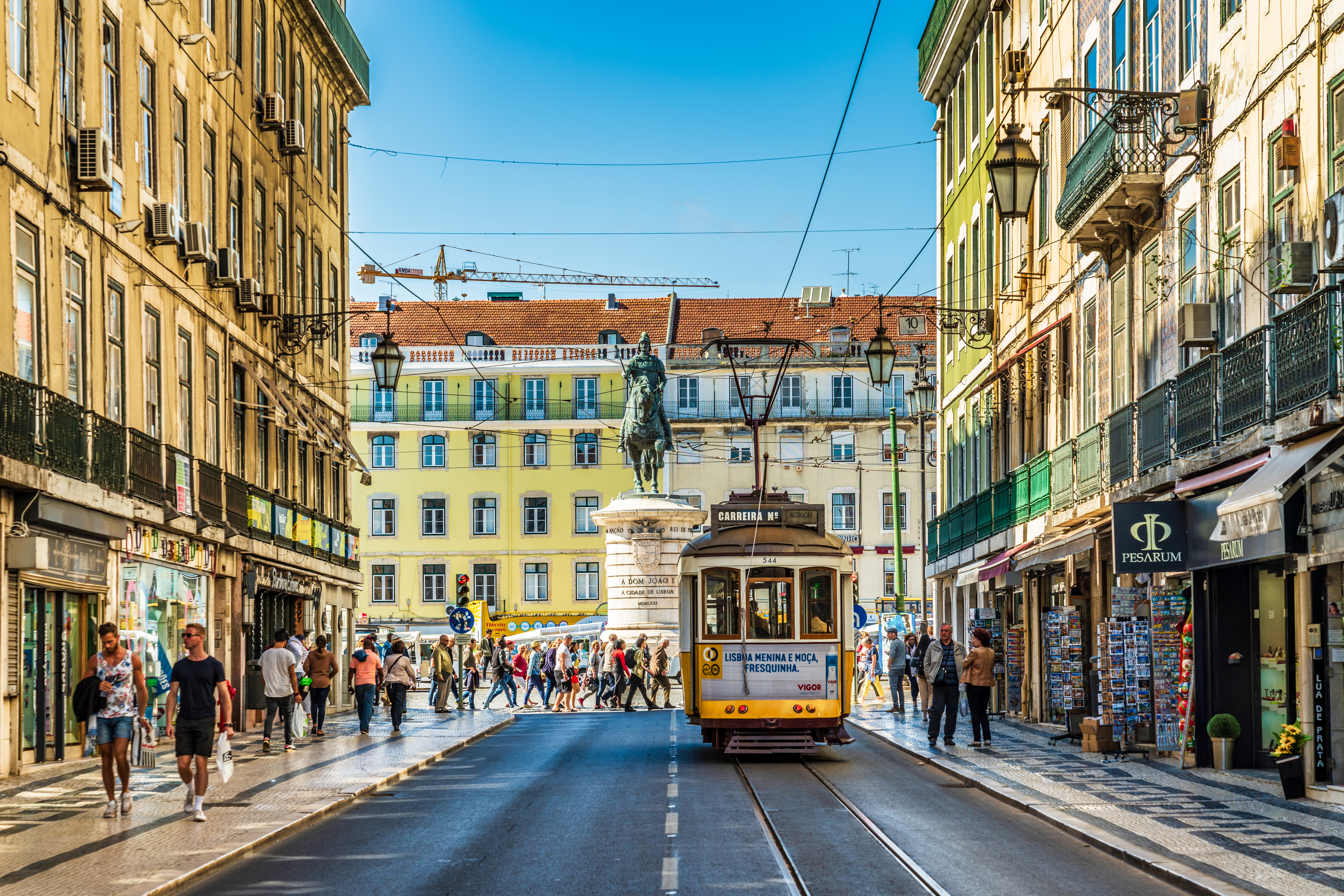 Historic yellow tram on a bustling Lisbon street with people and colorful buildings.