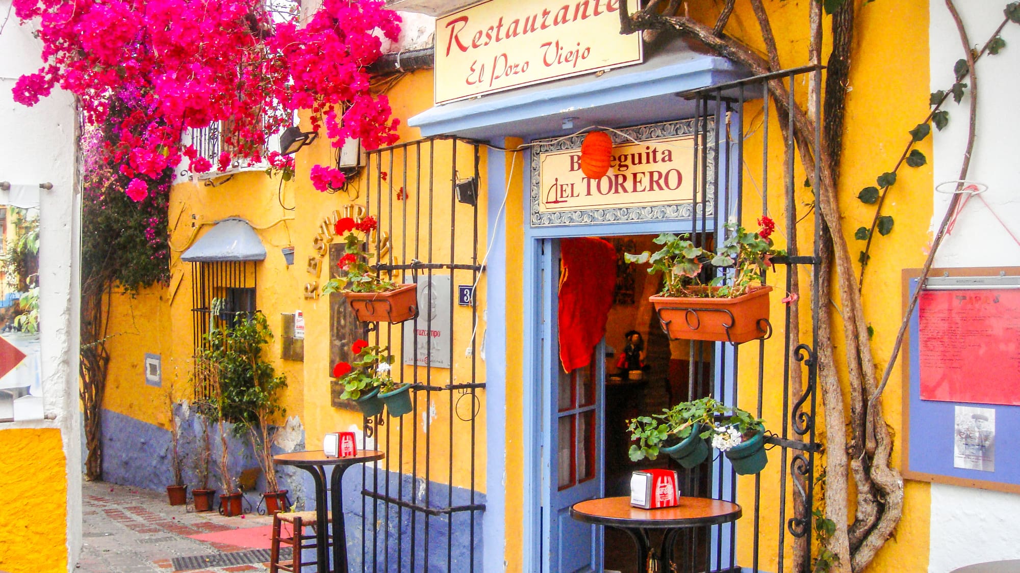 a yellow building with a sign and tables and chairs