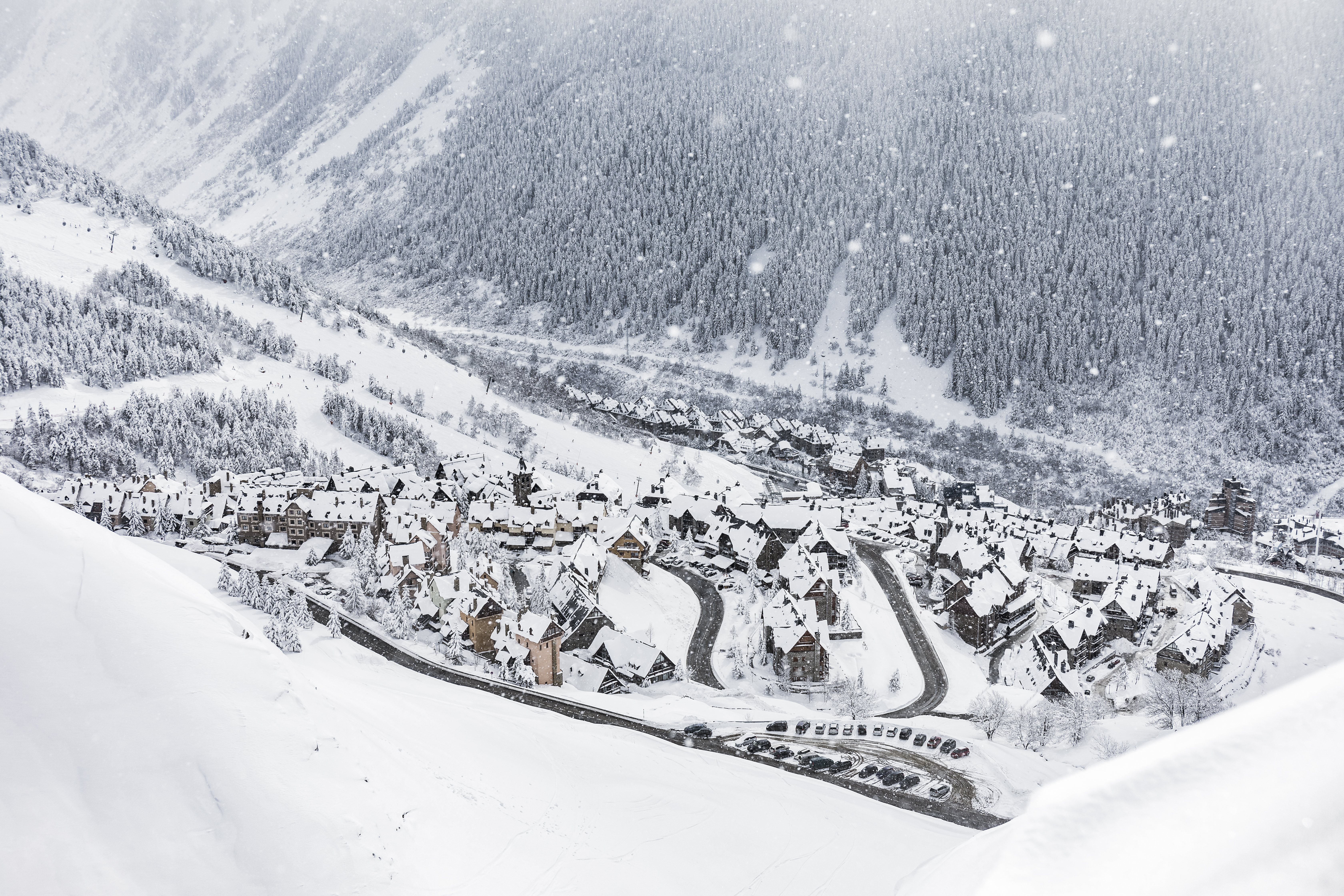 Snow-covered alpine village and winding roads in a mountain forest valley.
