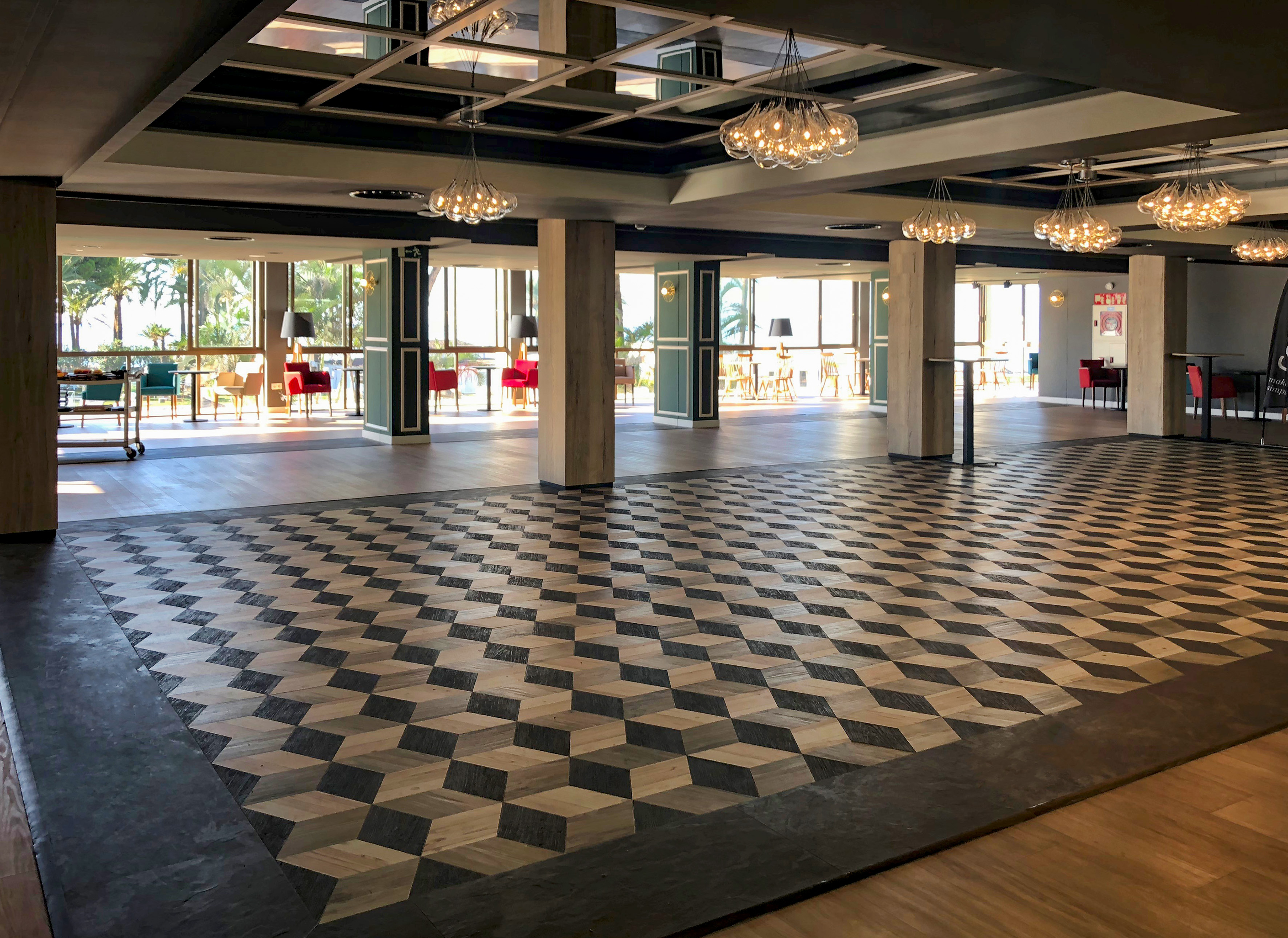 Hotel lobby with geometric cube floor, ocean view, and modern chandeliers.