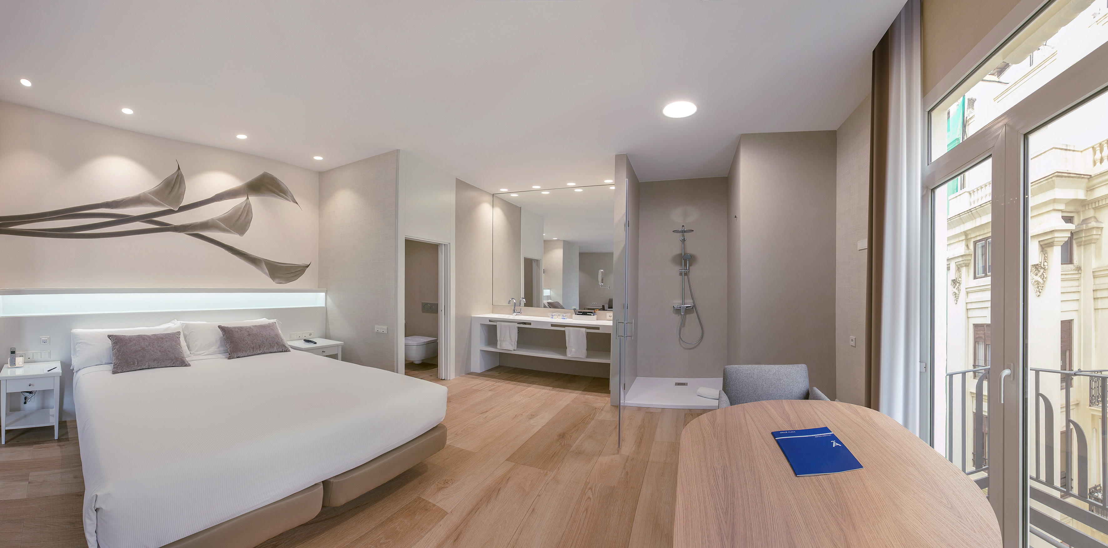 Modern hotel room with bed, open-plan bathroom, wooden floor, and balcony.