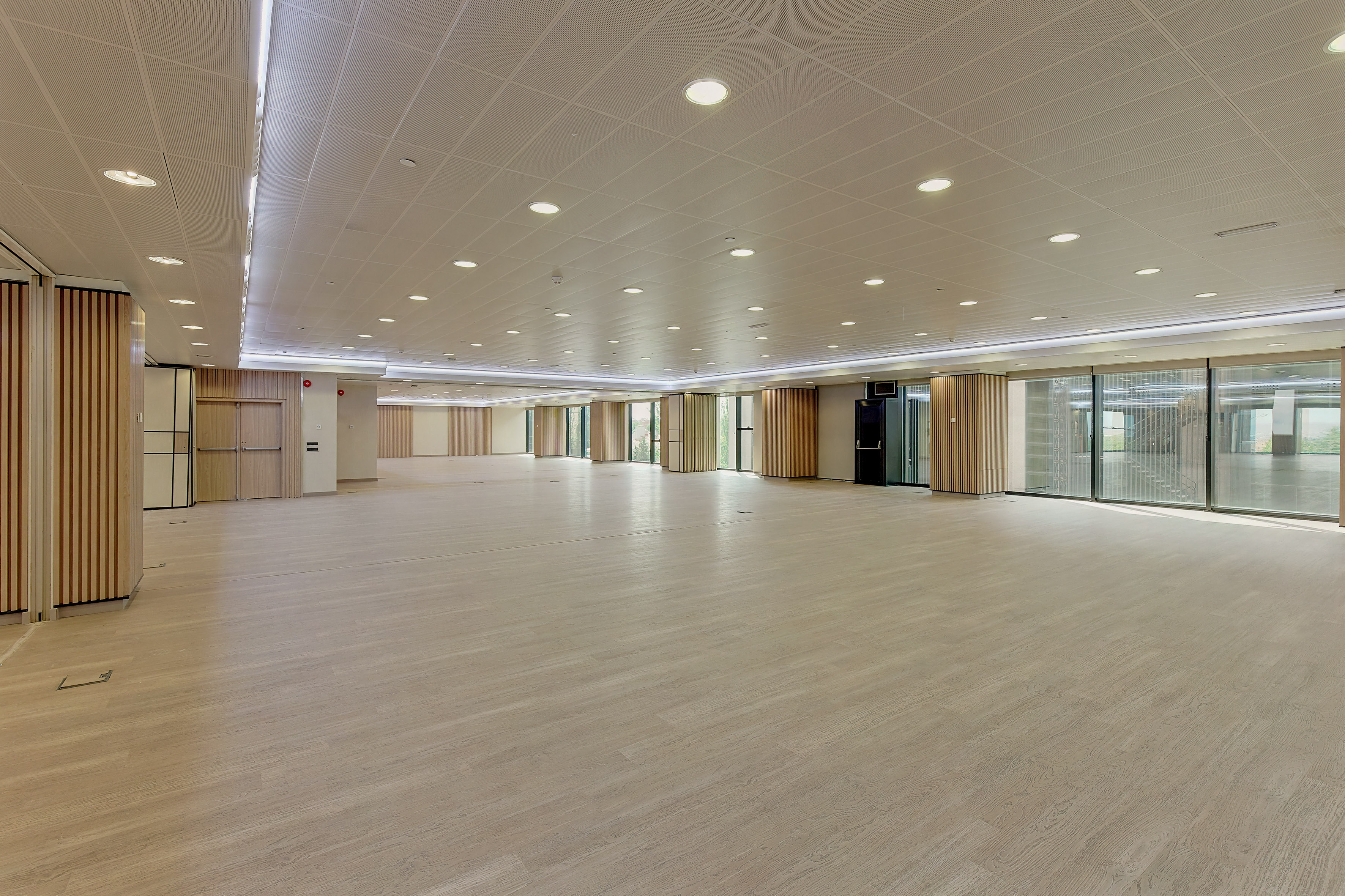 Modern empty event space with light wood floor and bright overhead lighting.