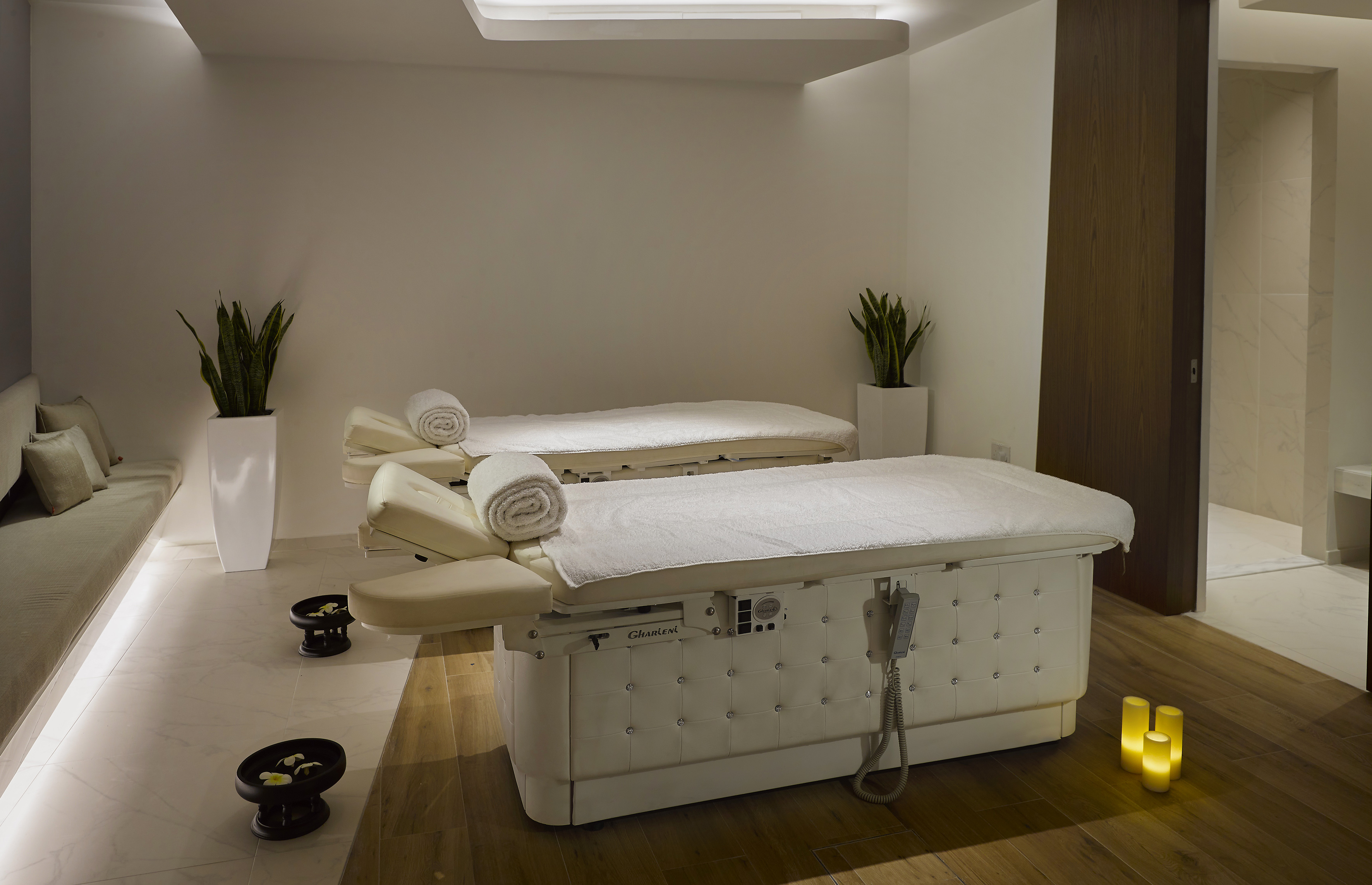 Modern spa treatment room with two Gharieni massage beds, plants, and soft lighting.