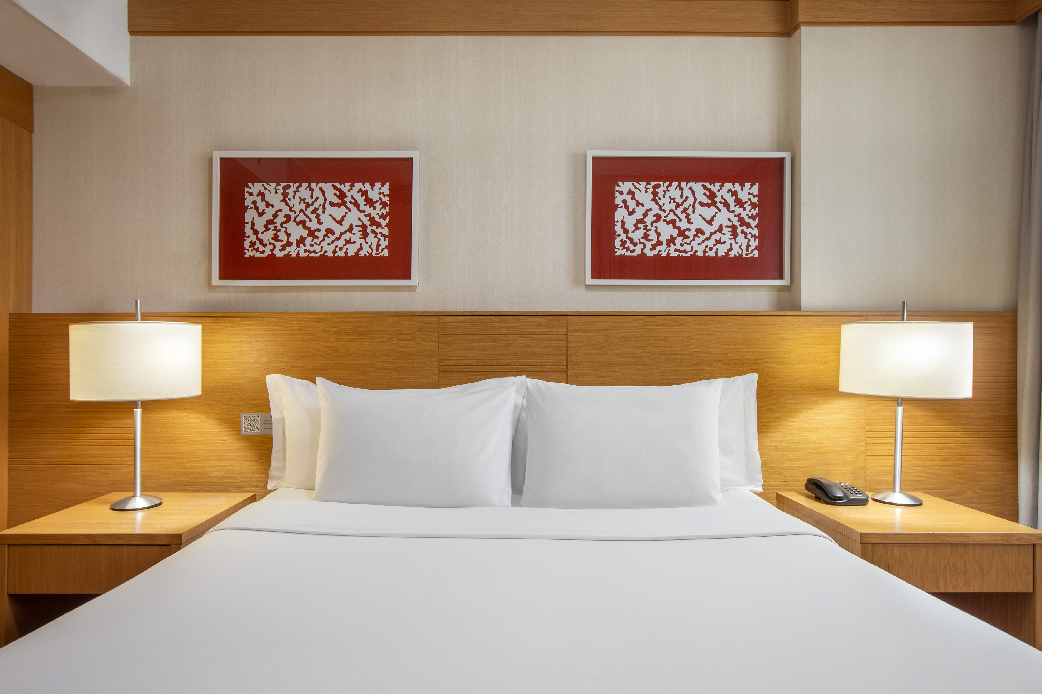 Hotel room with white bed, wooden headboard, lamps, and red abstract art.