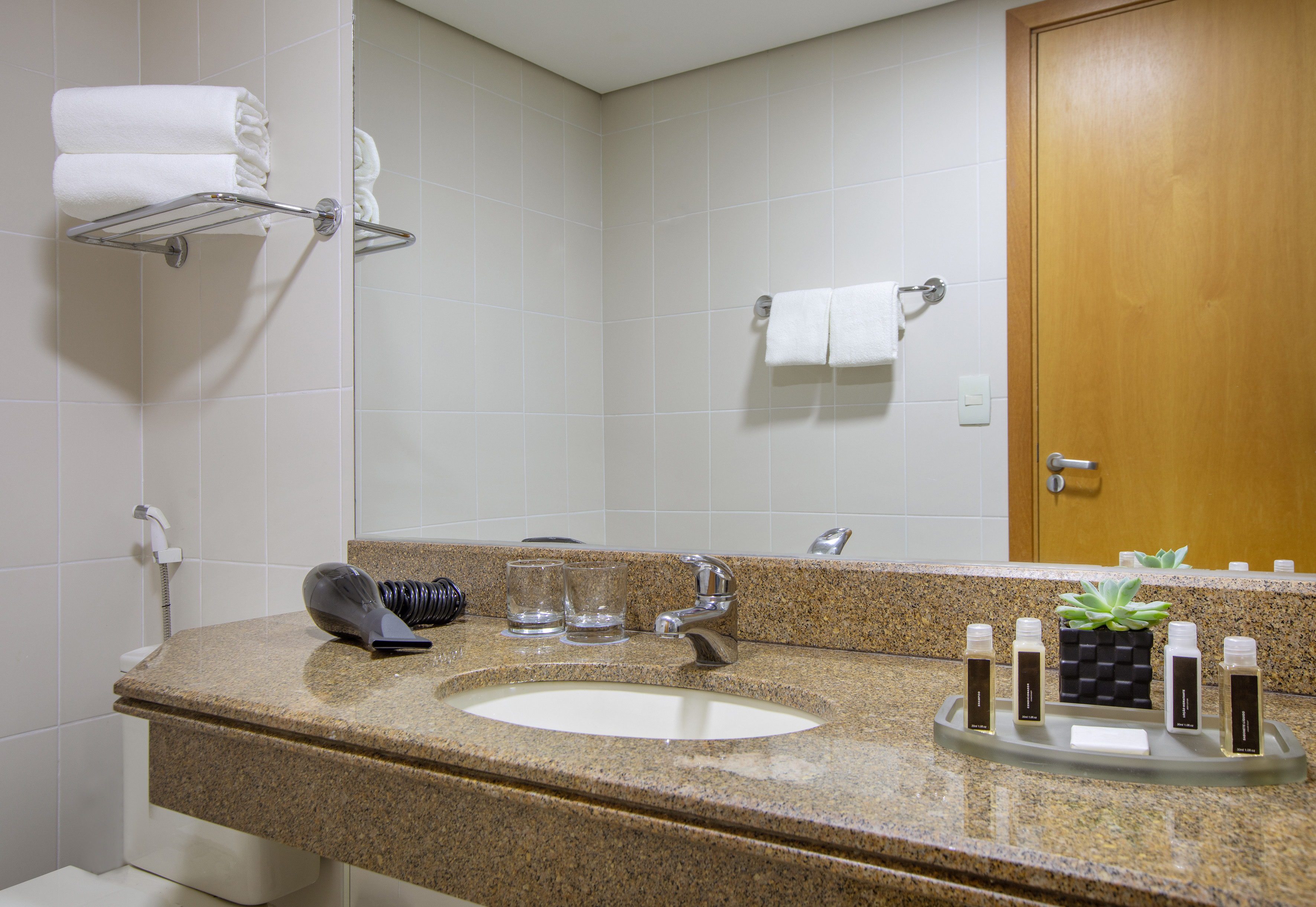 Modern hotel bathroom with granite vanity, sink, mirror, towels, and toiletries.