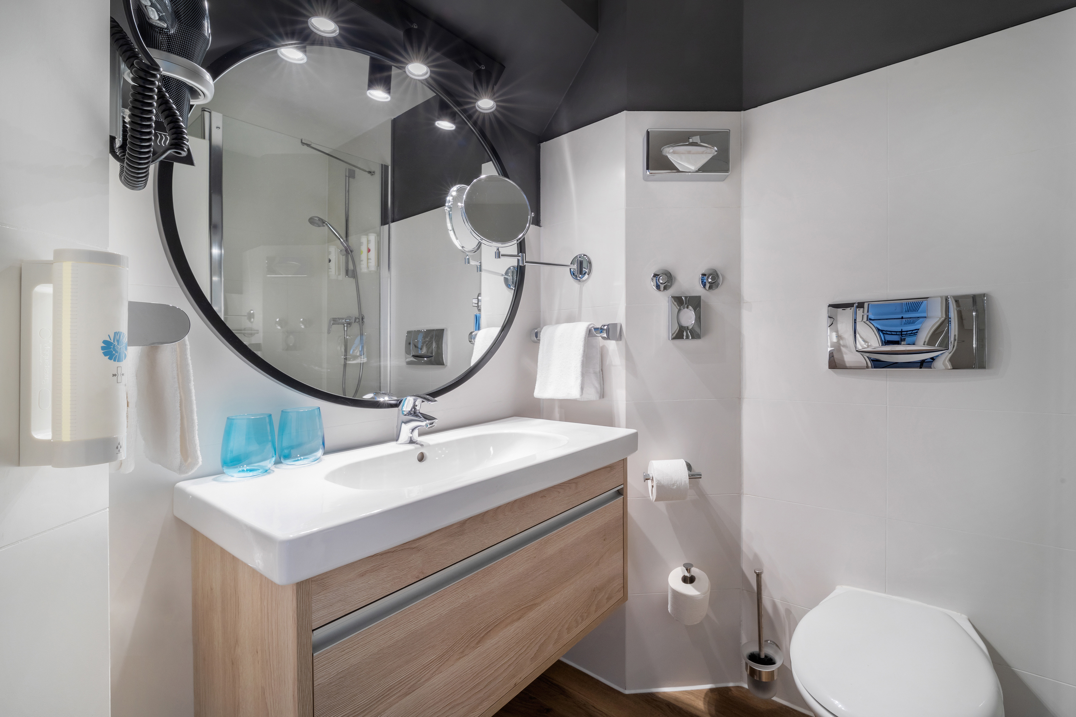 Modern hotel bathroom with wood vanity, round mirror, white sink, and shower.