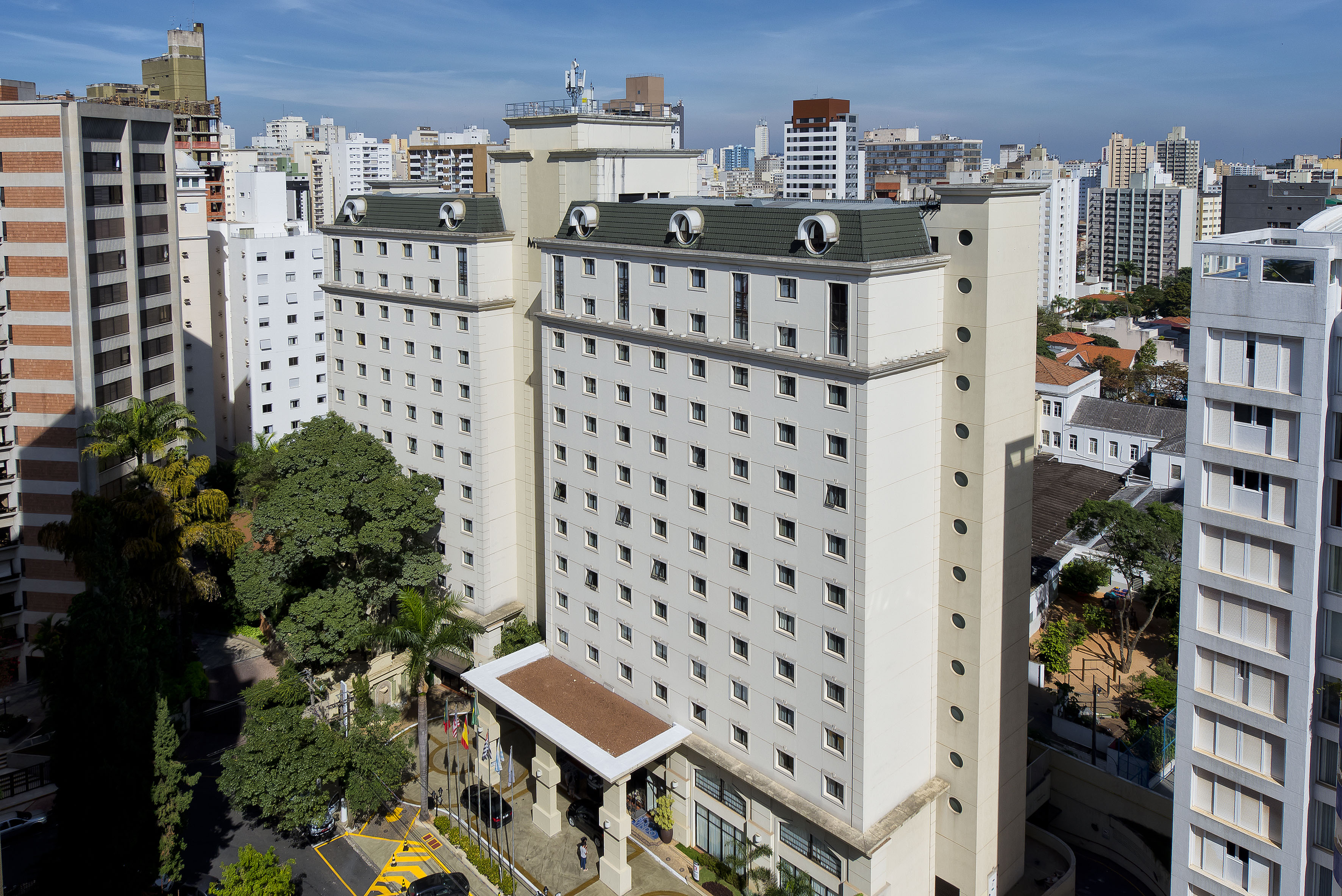 White hotel building with dormer windows and green roof in a dense city environment.