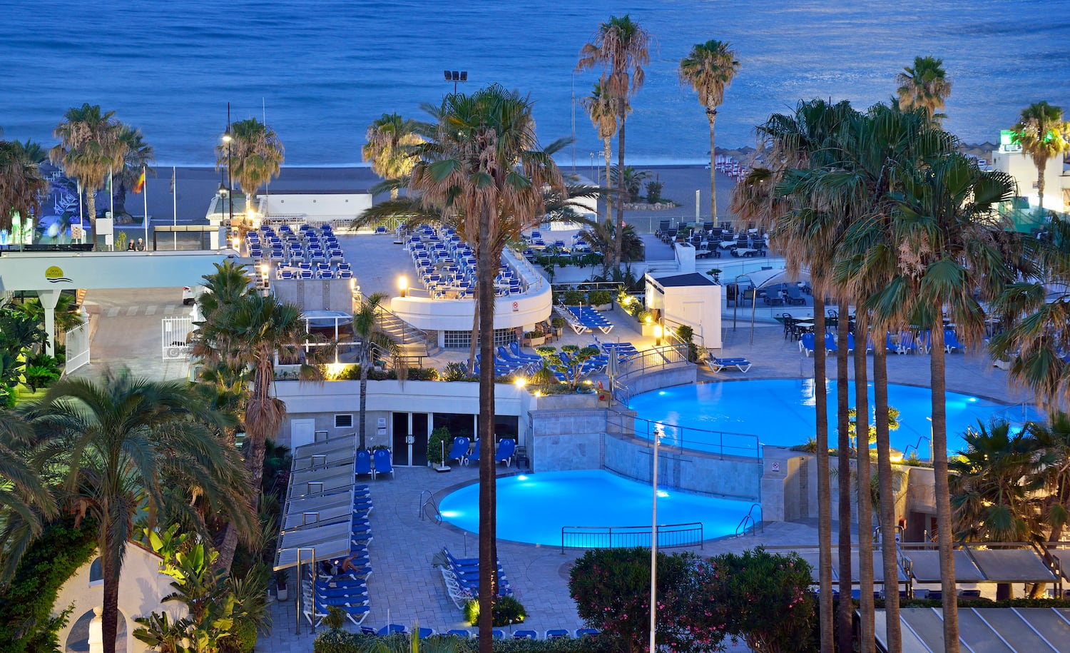 a pool with palm trees and a building with a beach and water