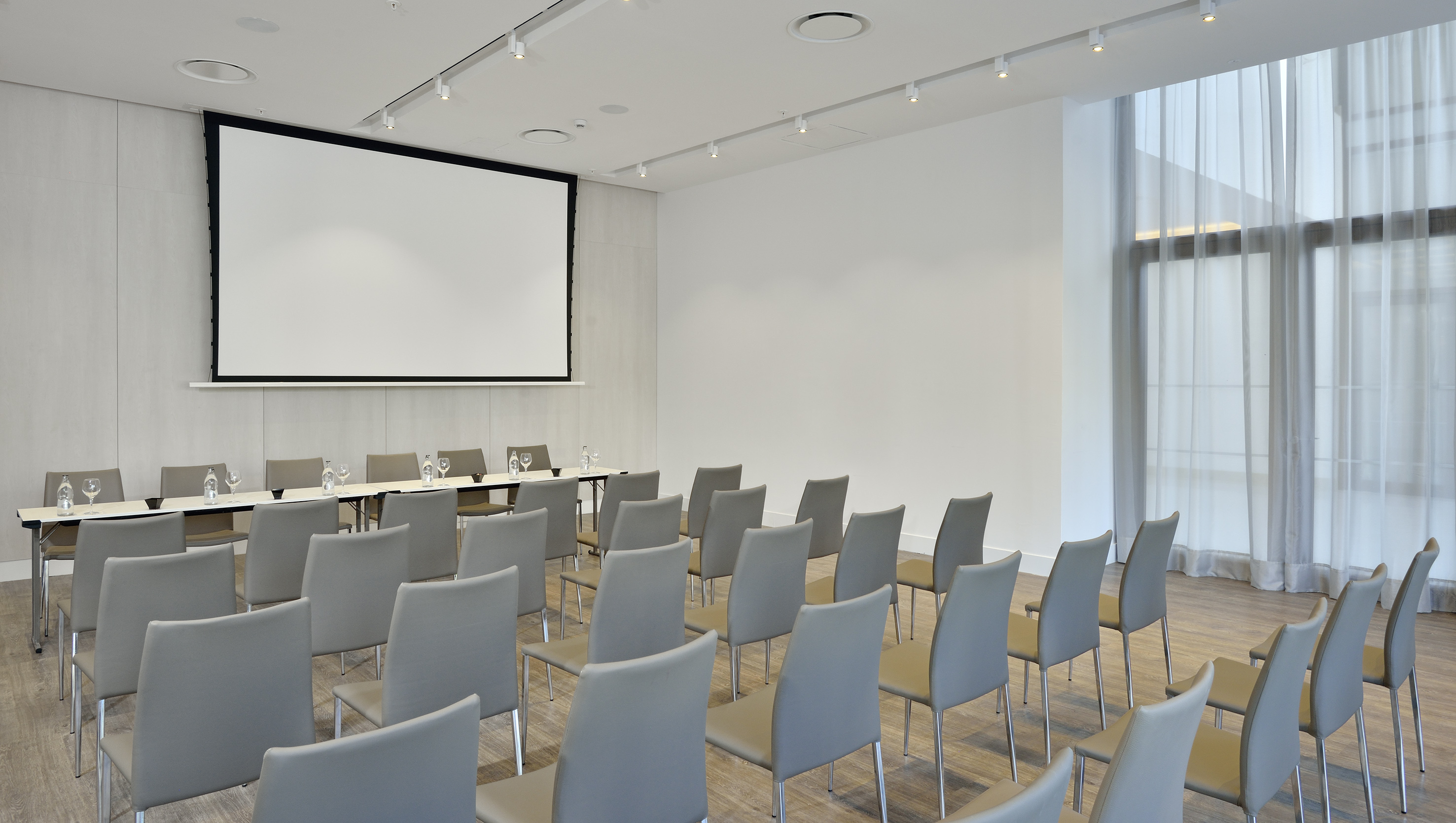 Modern, empty conference room with grey chairs, tables, and projection screen.