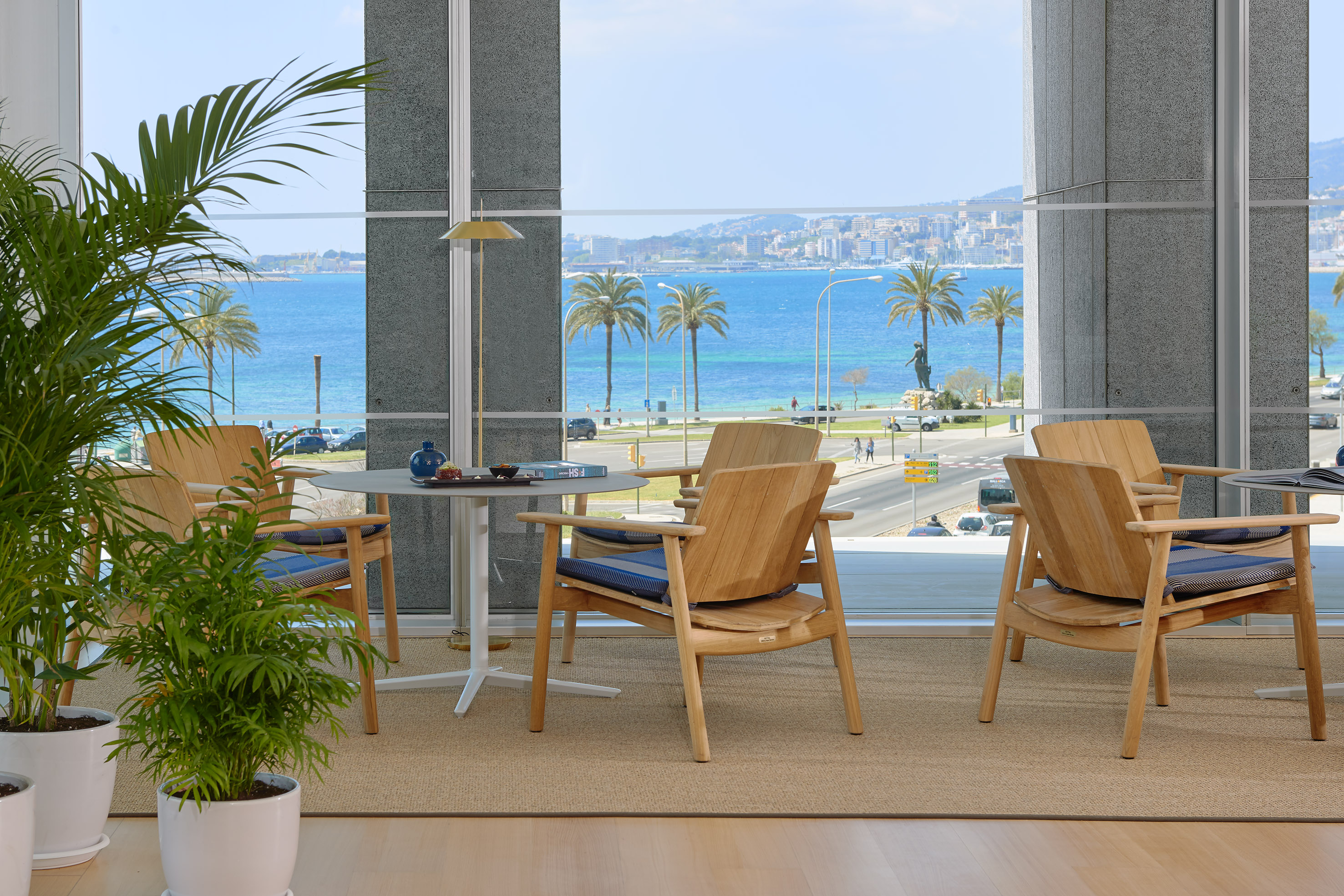 Coastal lounge with wooden chairs, plants, and panoramic sea view.