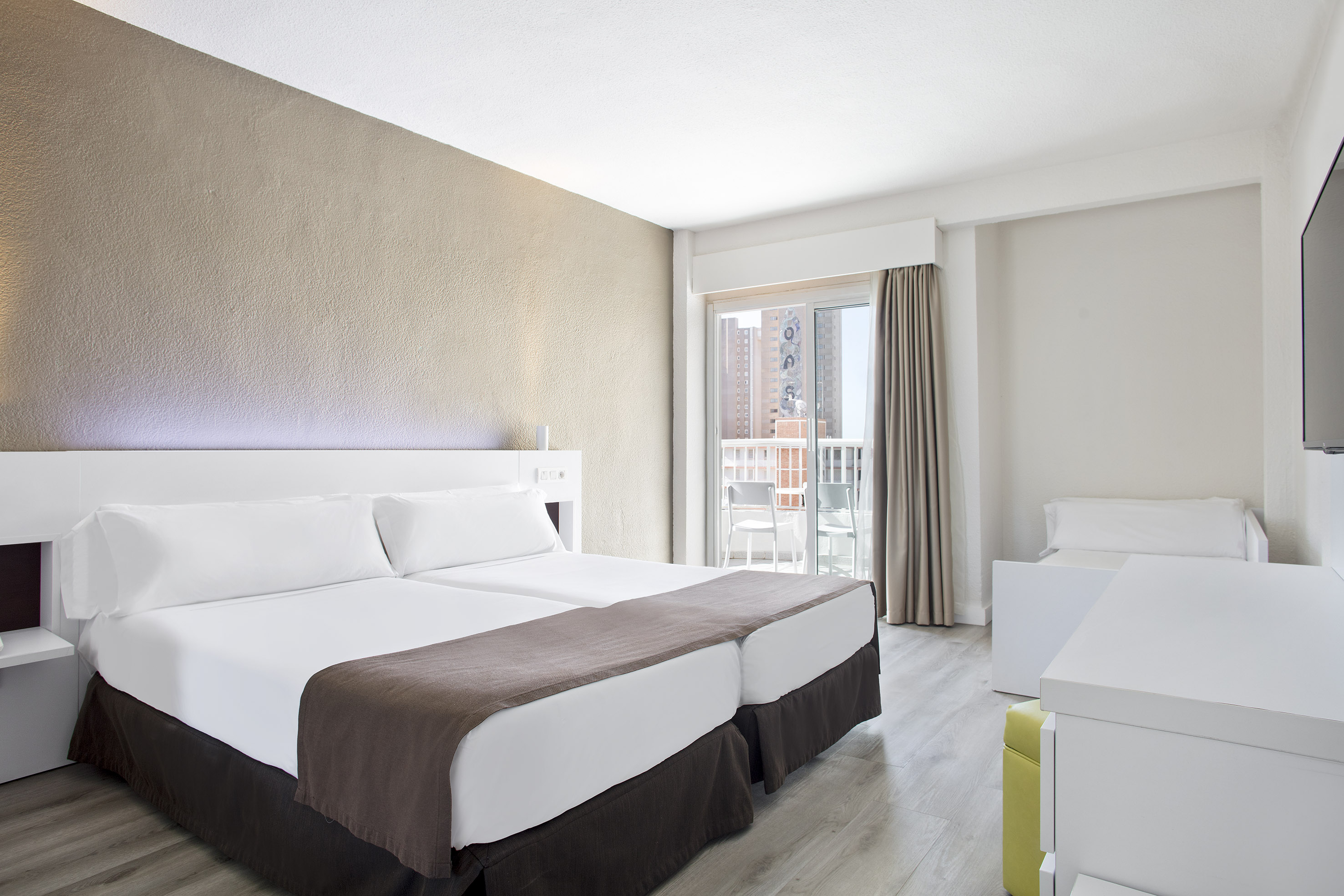 Twin bed hotel room with balcony, modern decor, and city view.