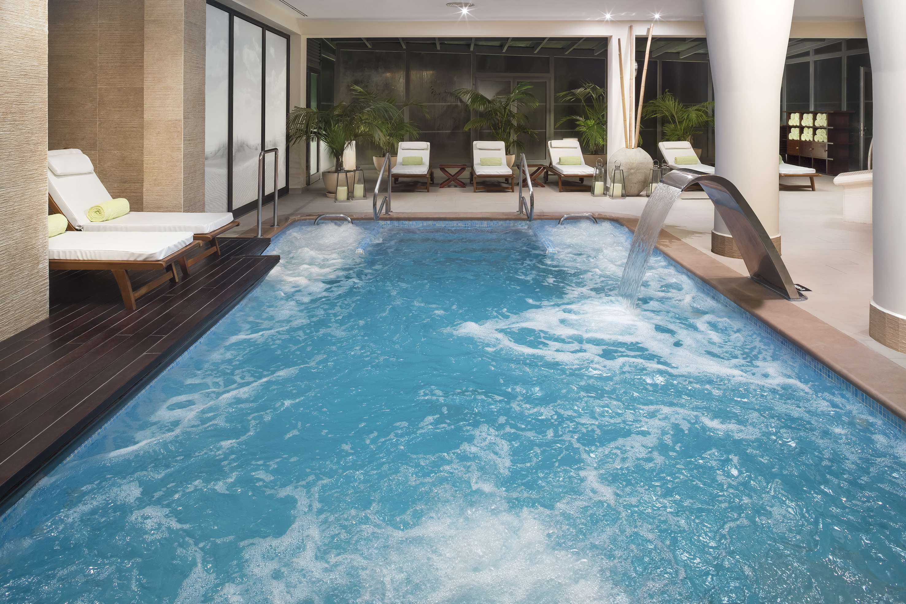 Indoor spa pool with waterfall, bubbling water, and lounge chairs.
