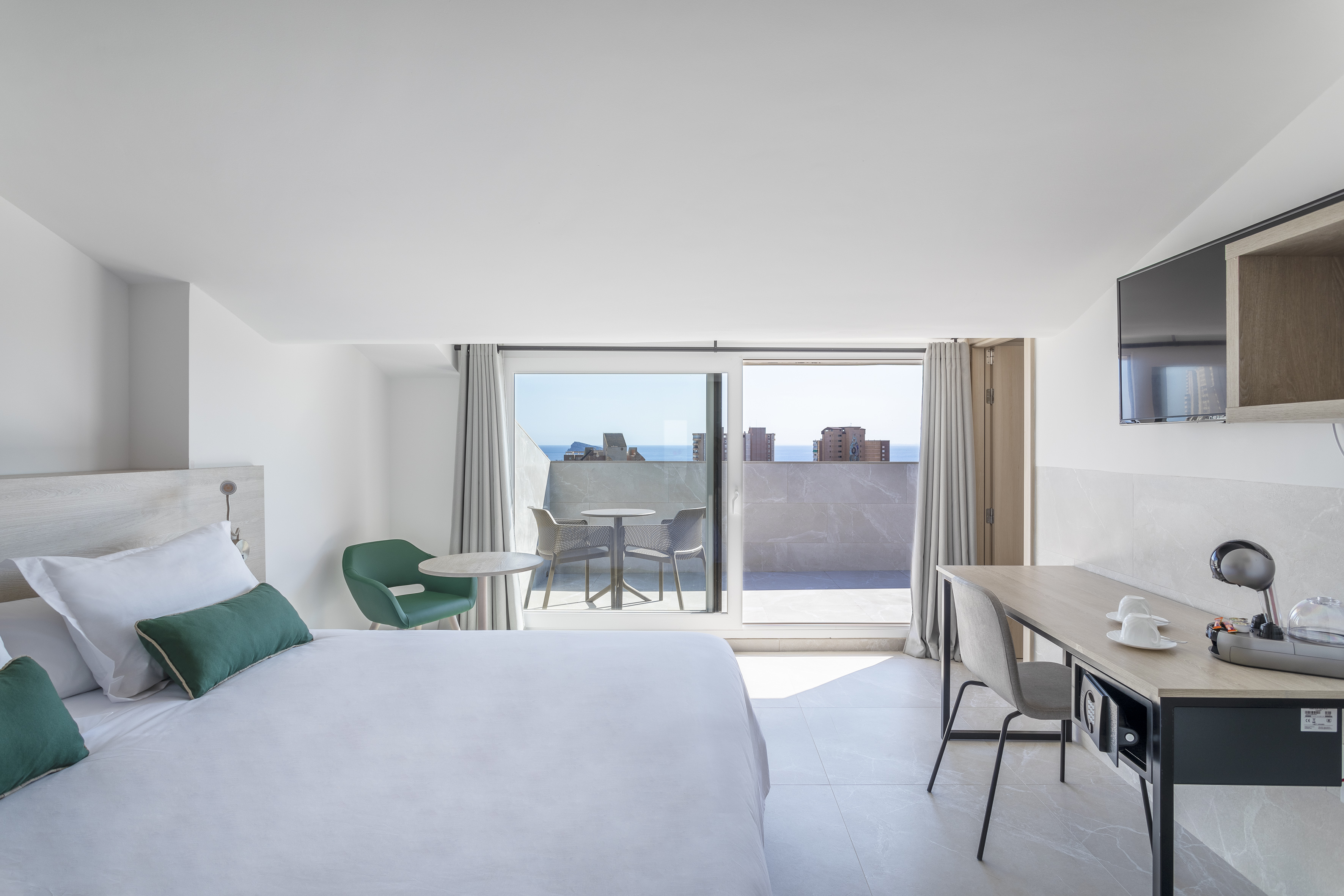 Modern hotel room with ocean view balcony, white bed, and modern workspace.