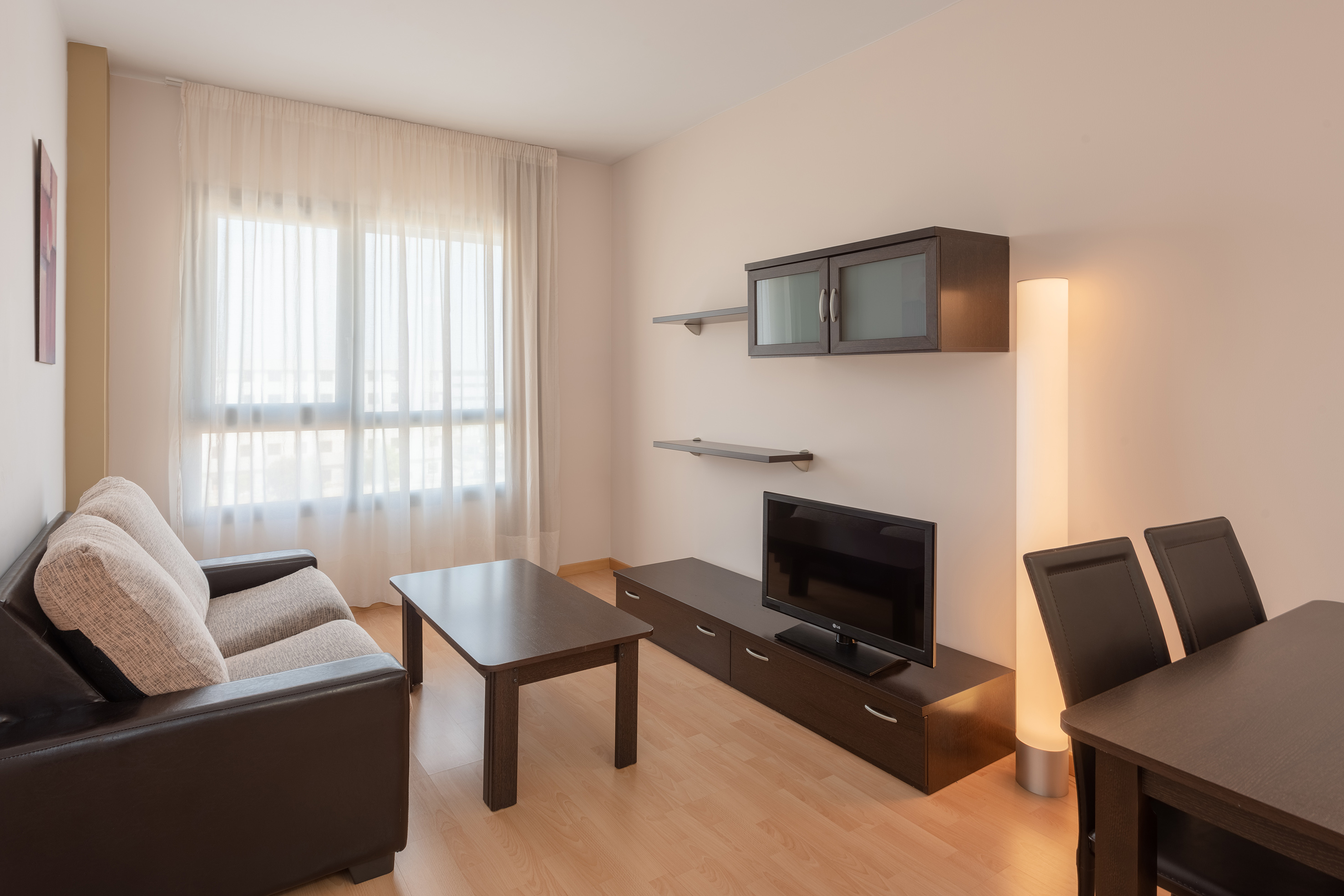 Modern apartment living room with sofa, TV, dining area, and wood floor.