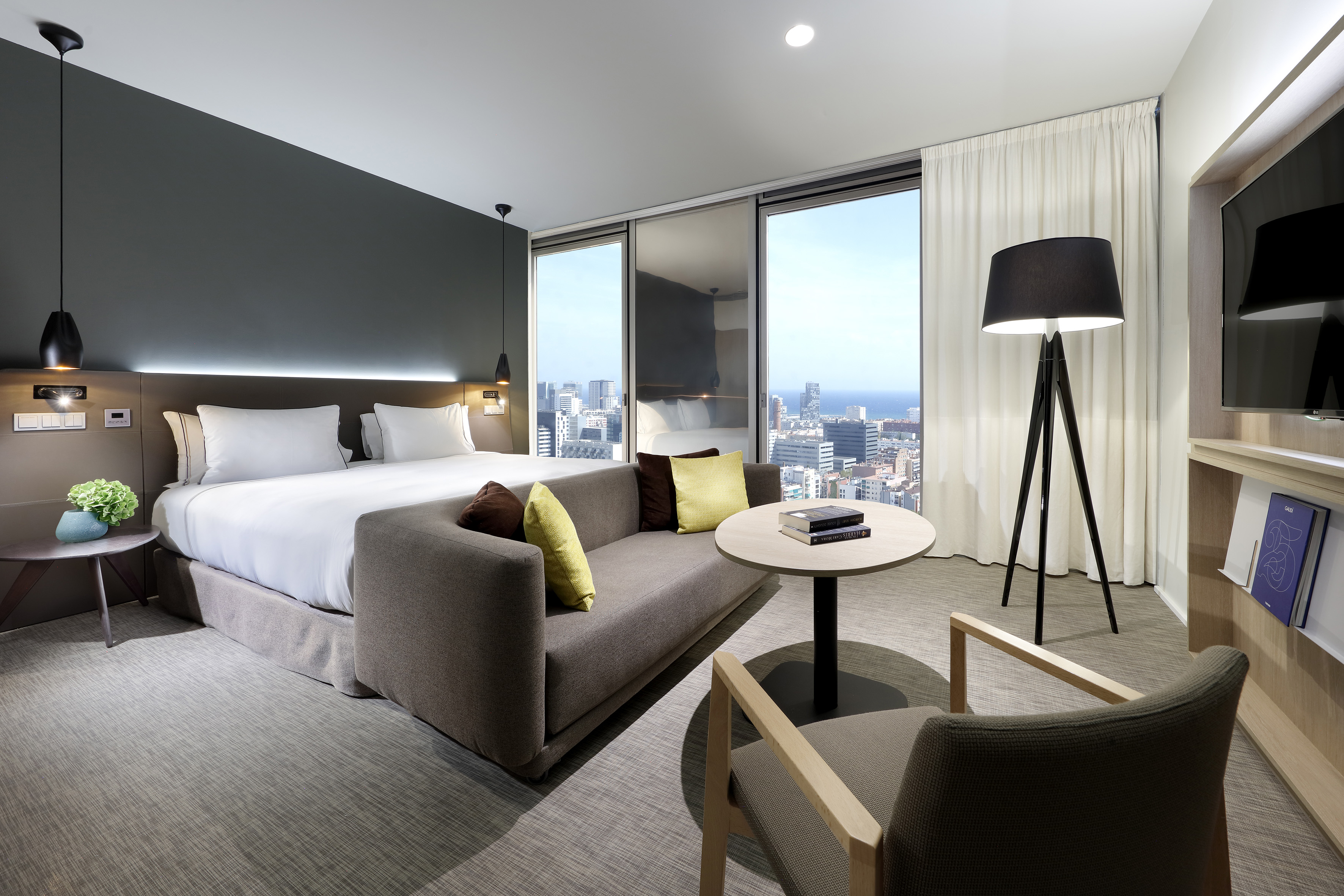 Luxury hotel room with king bed, sofa, and panoramic city-ocean views.