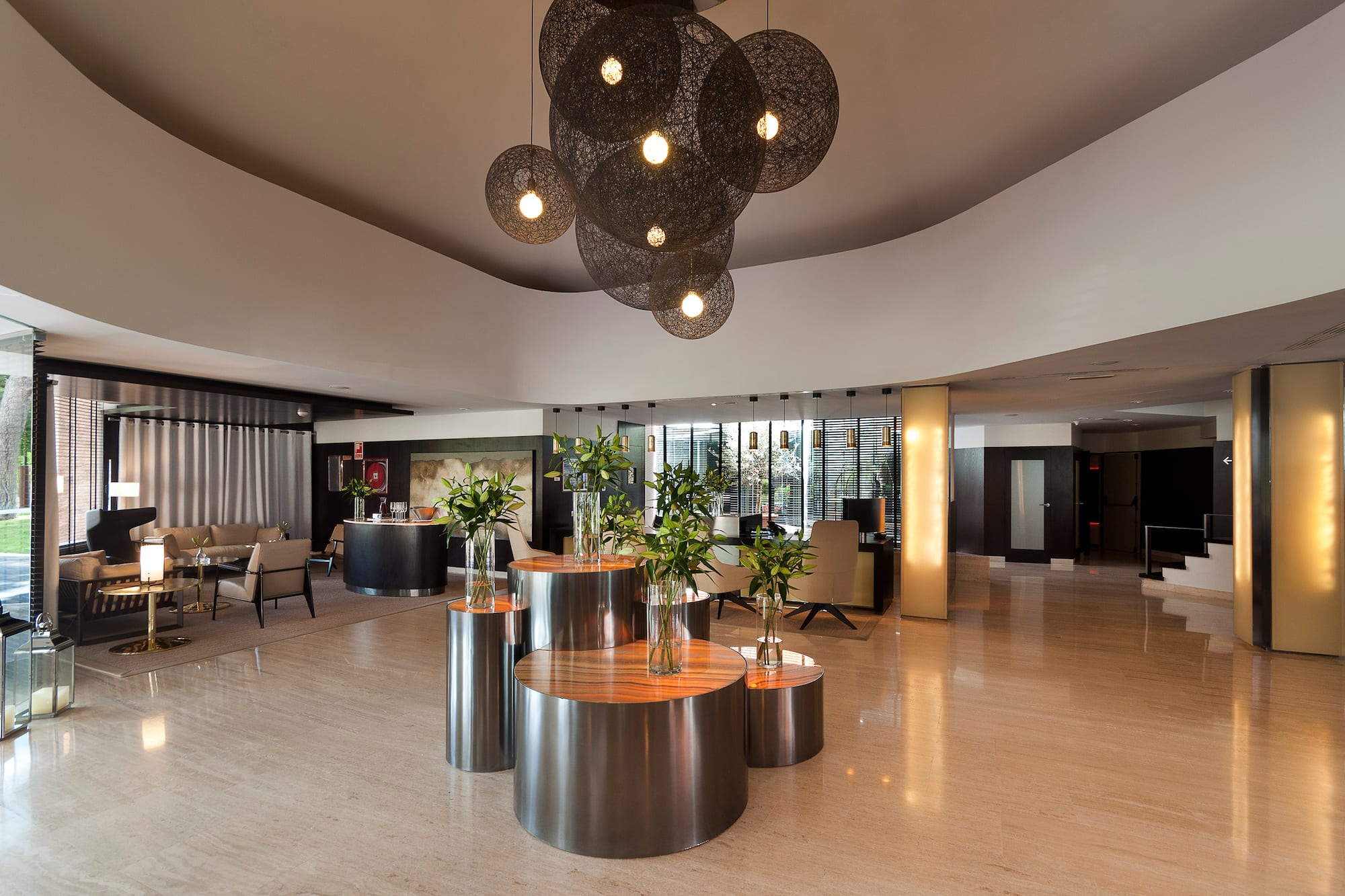 Modern hotel lobby with stylish spherical chandeliers, marble floor, and lounge.