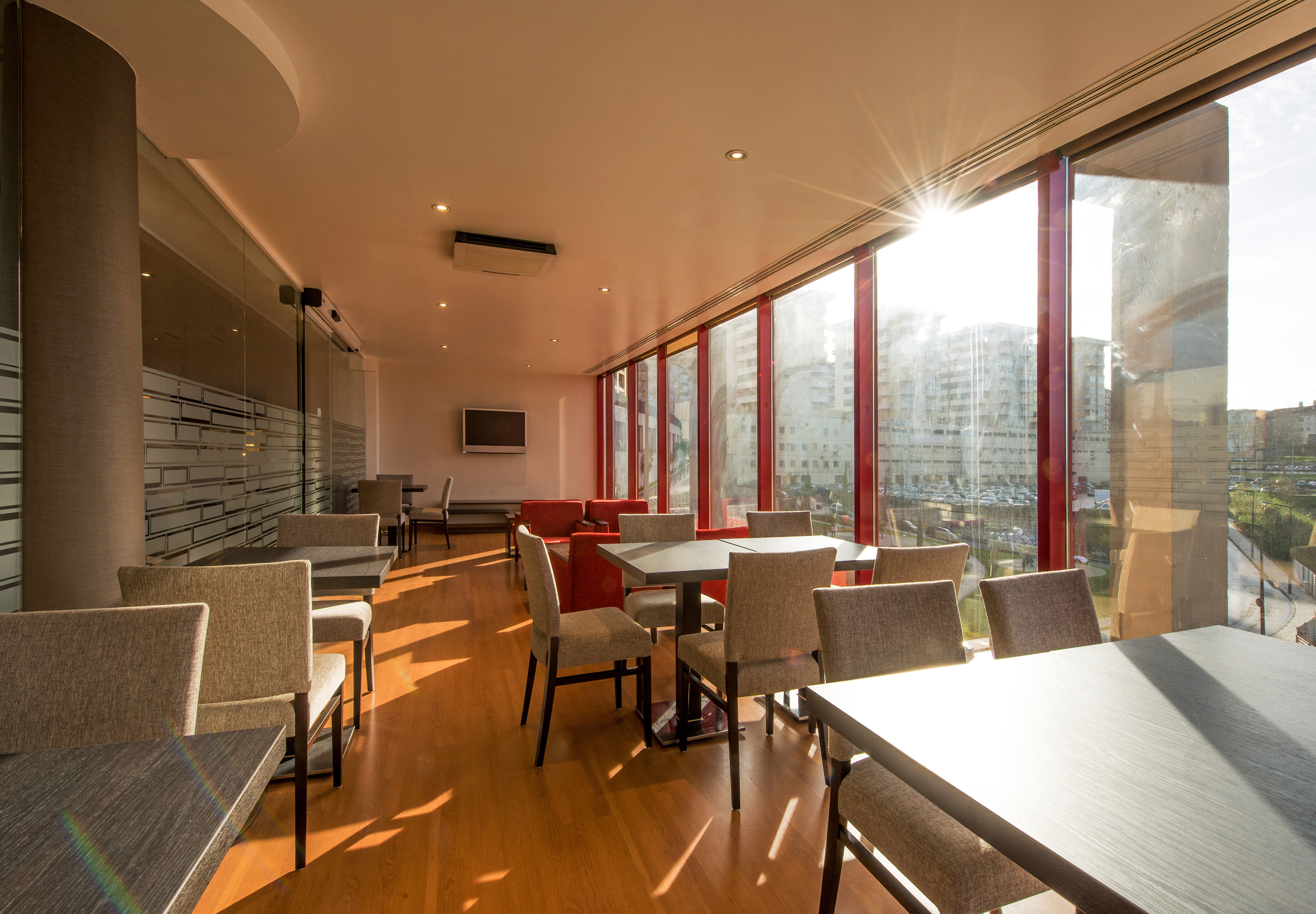 Sunlit modern dining area with wooden floor, tables, and large windows.