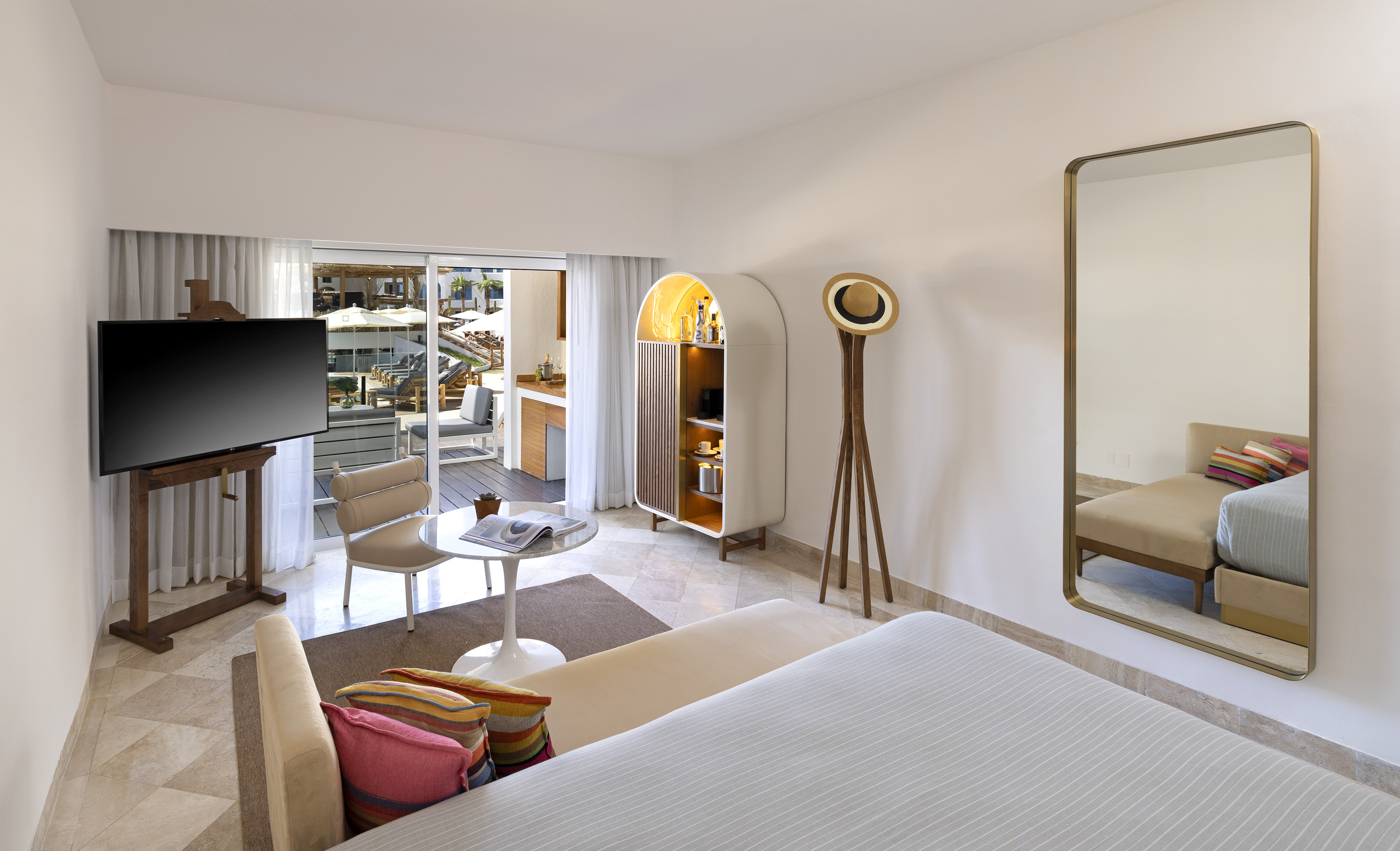 Modern hotel suite with private balcony, large TV, and contemporary minibar cabinet.