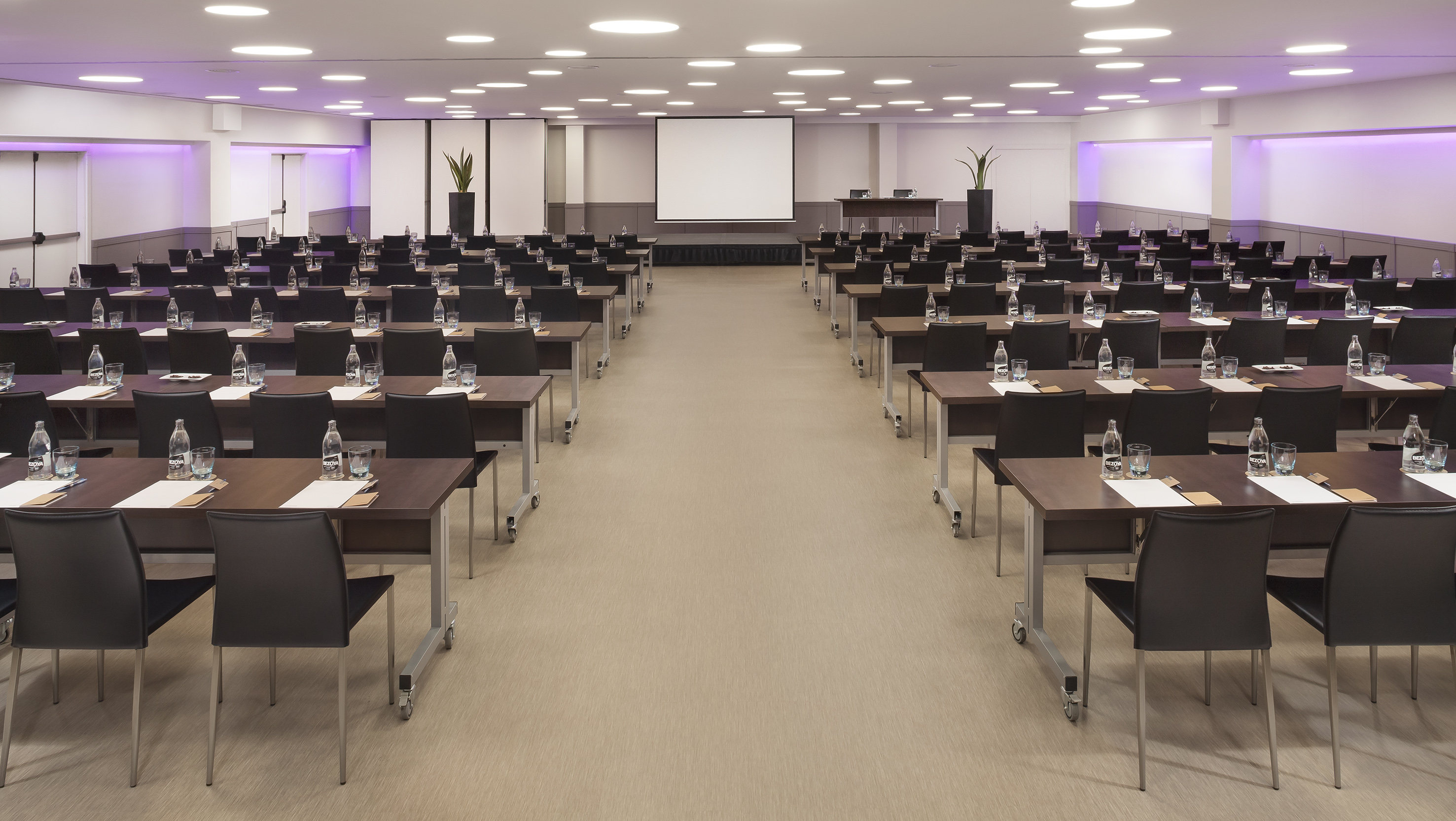 Modern conference room with tables, chairs, water bottles, and projector screen.