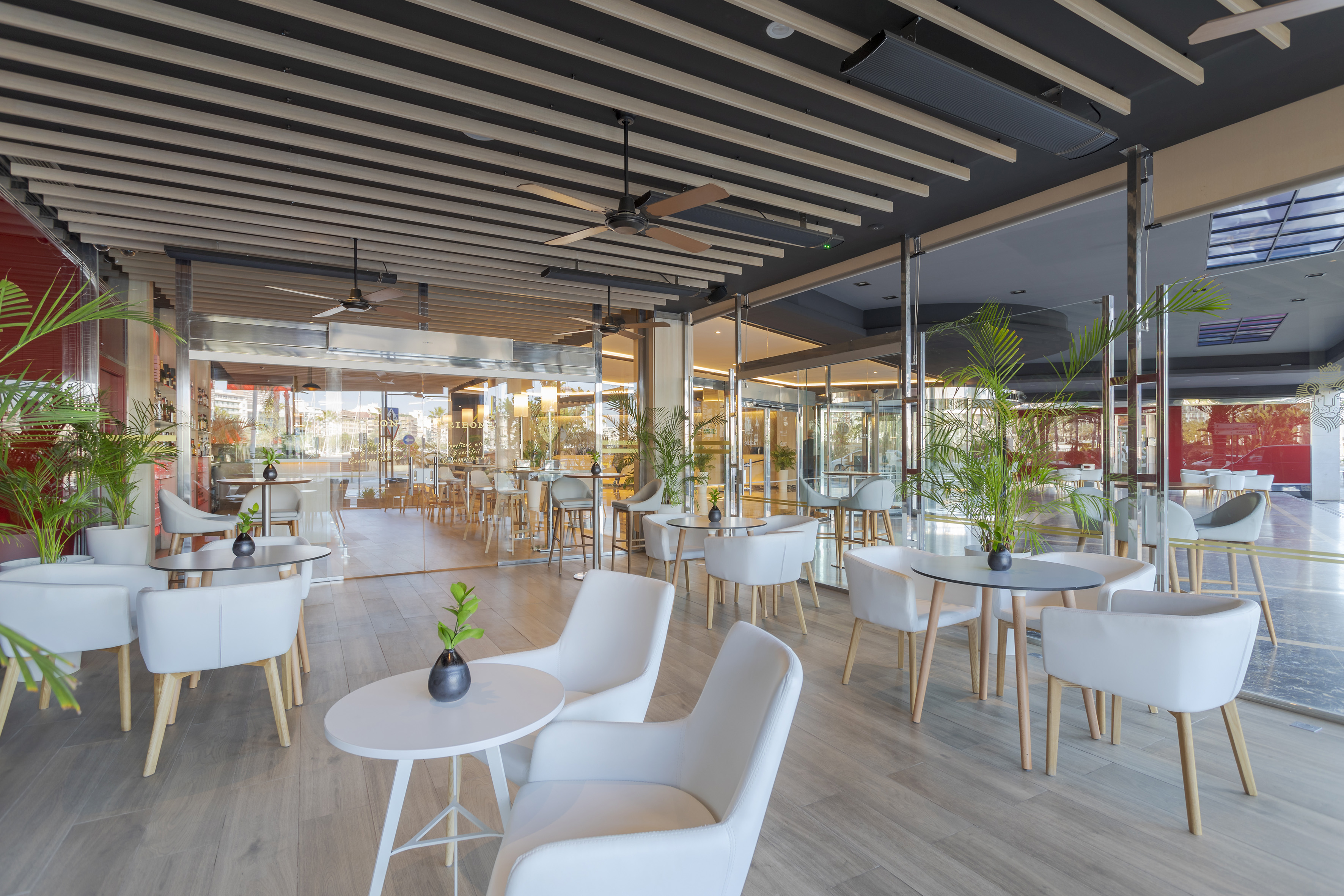 Bright contemporary cafe with white seating, wood tables, and lush plants.