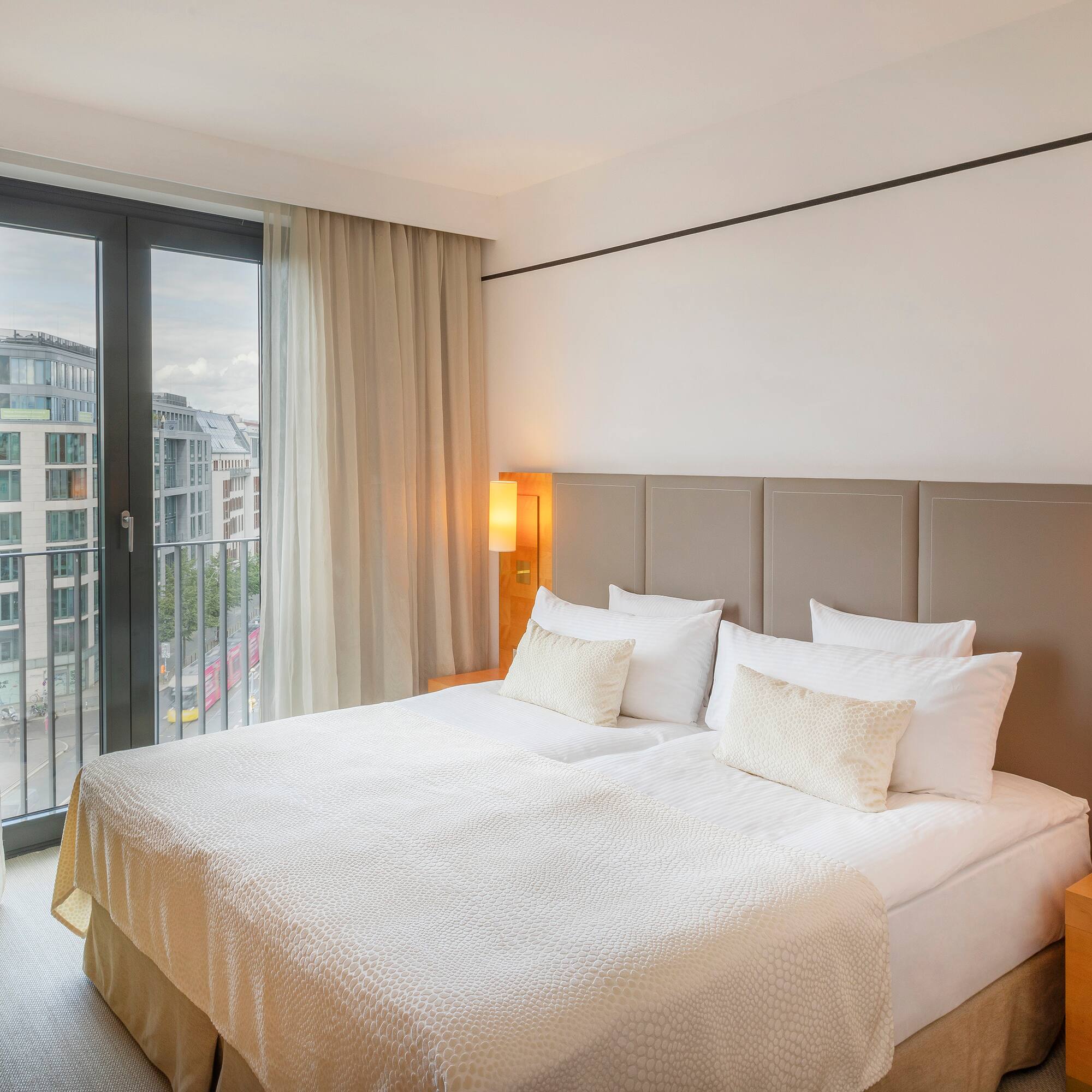Modern hotel bedroom with city view, large bed, and green armchair.