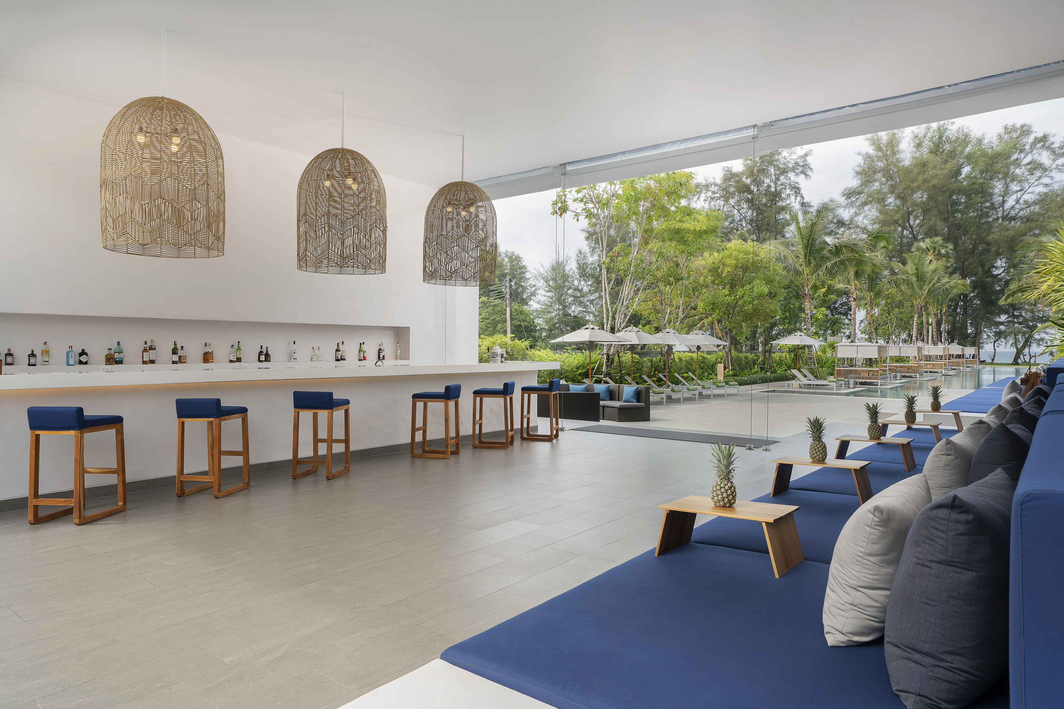 Modern poolside bar with blue lounge seating, woven lights, and tropical resort view.