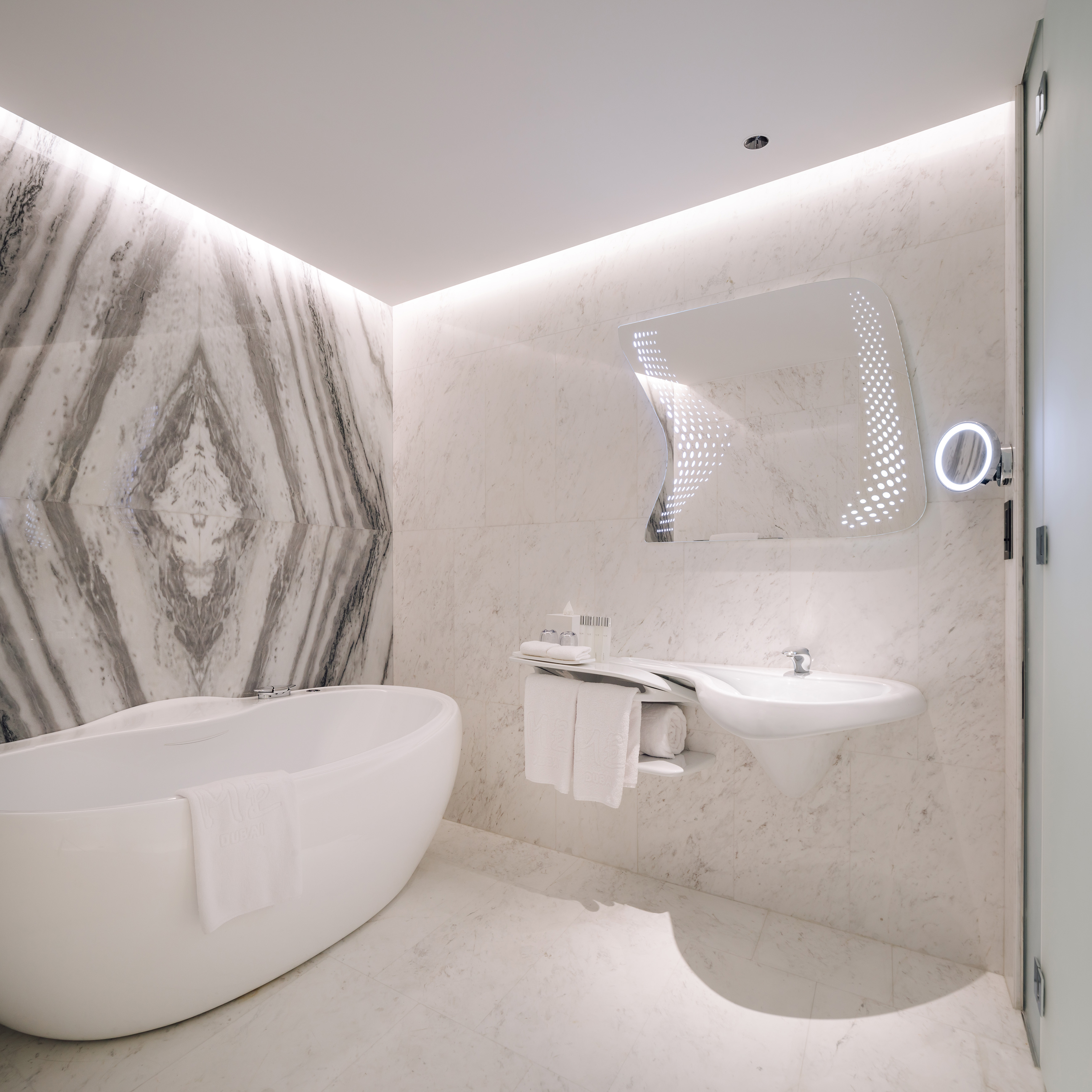 Luxury marble bathroom with freestanding tub, modern sink, and backlit mirror.