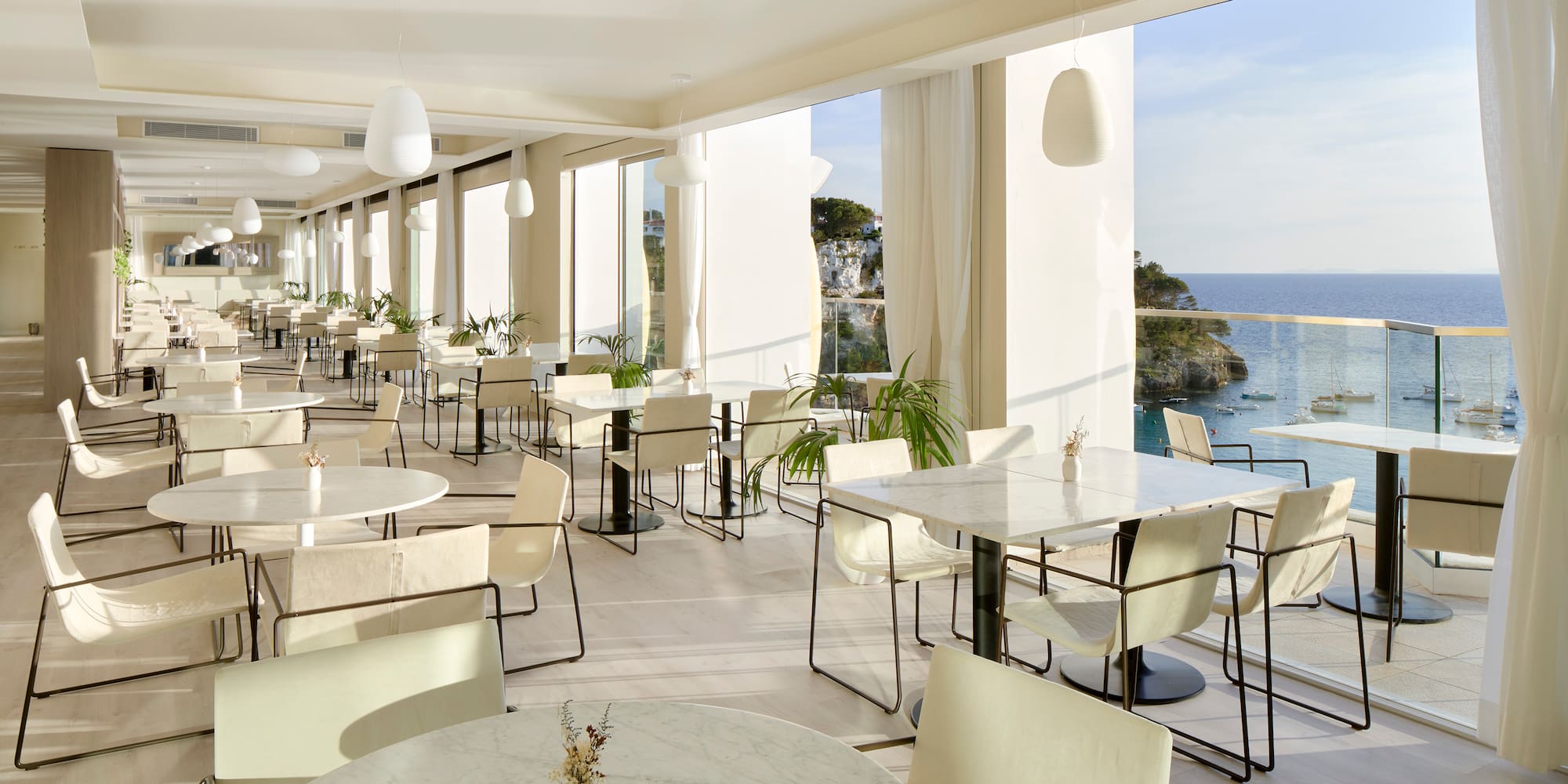 a room with tables and chairs and a view of the ocean