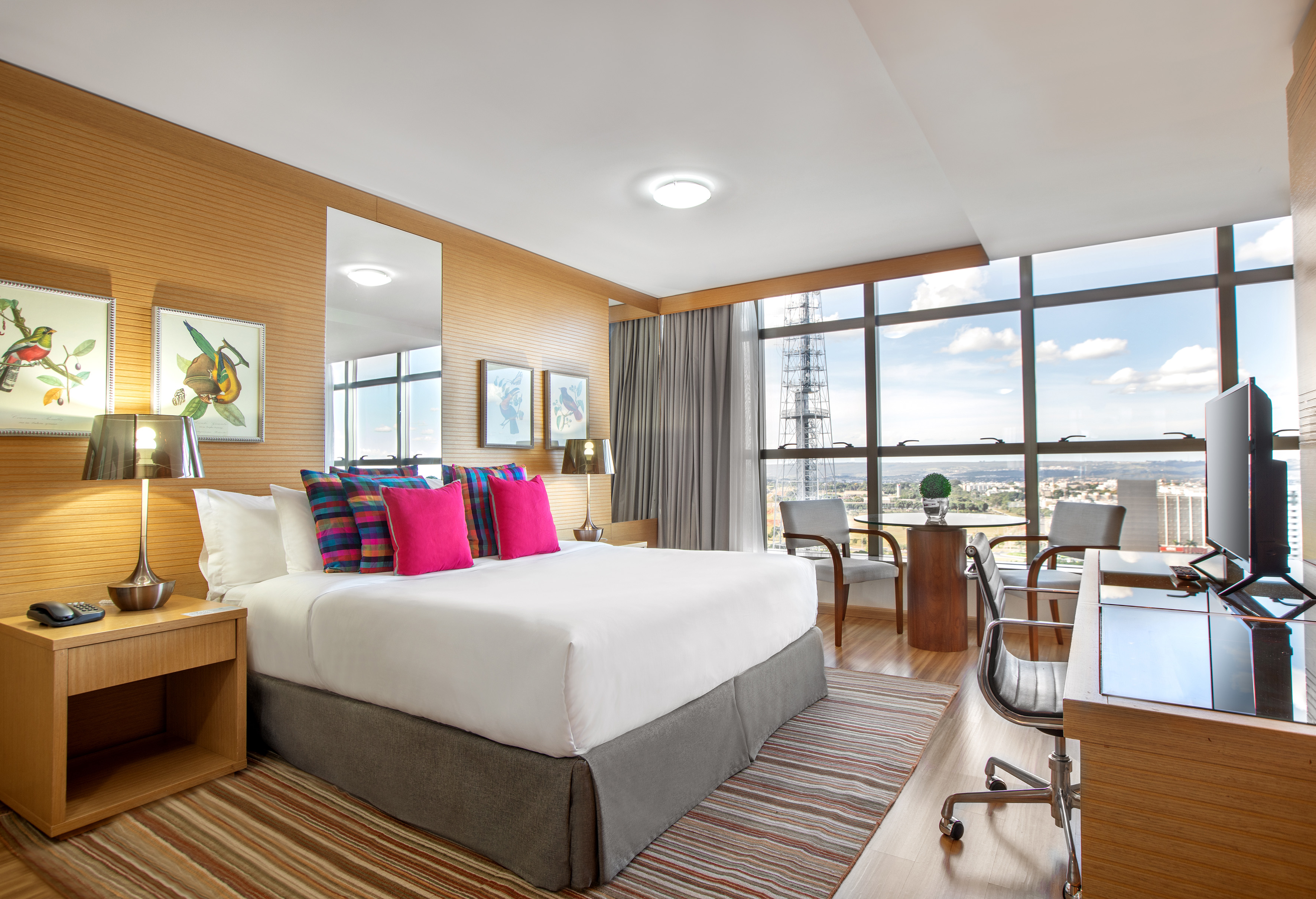 Bright hotel bedroom with city skyline view, king bed, and work desk.
