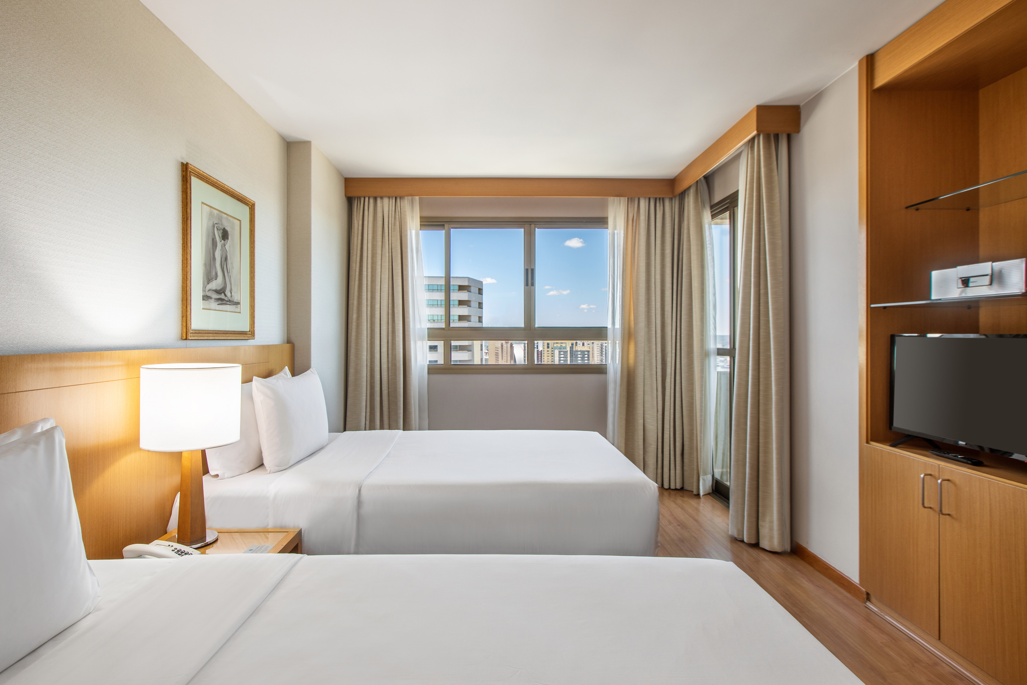 Bright hotel room with twin beds, city view, and wood details.