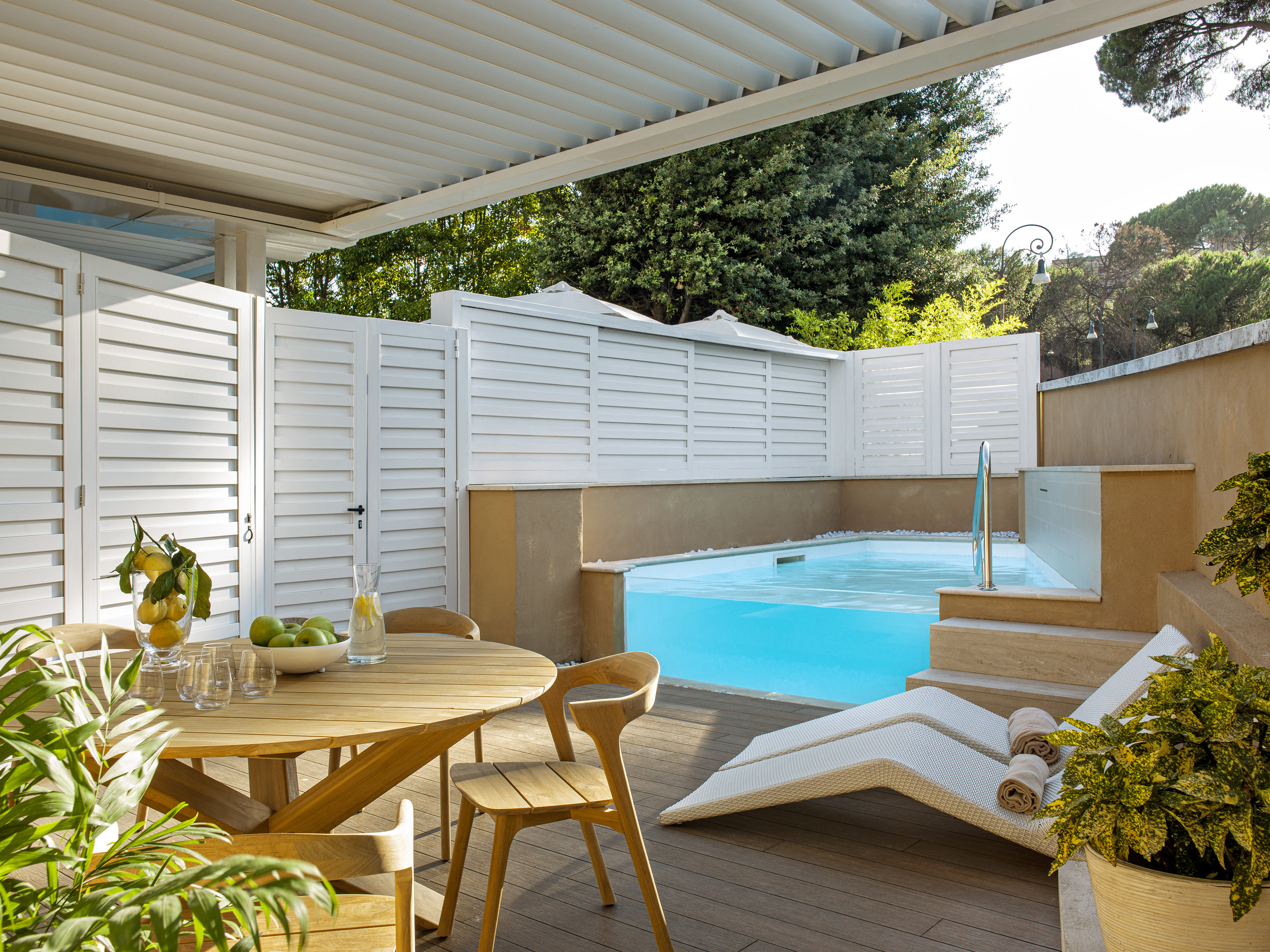 Private hotel patio with pool, outdoor dining, sun loungers, and shaded pergola.