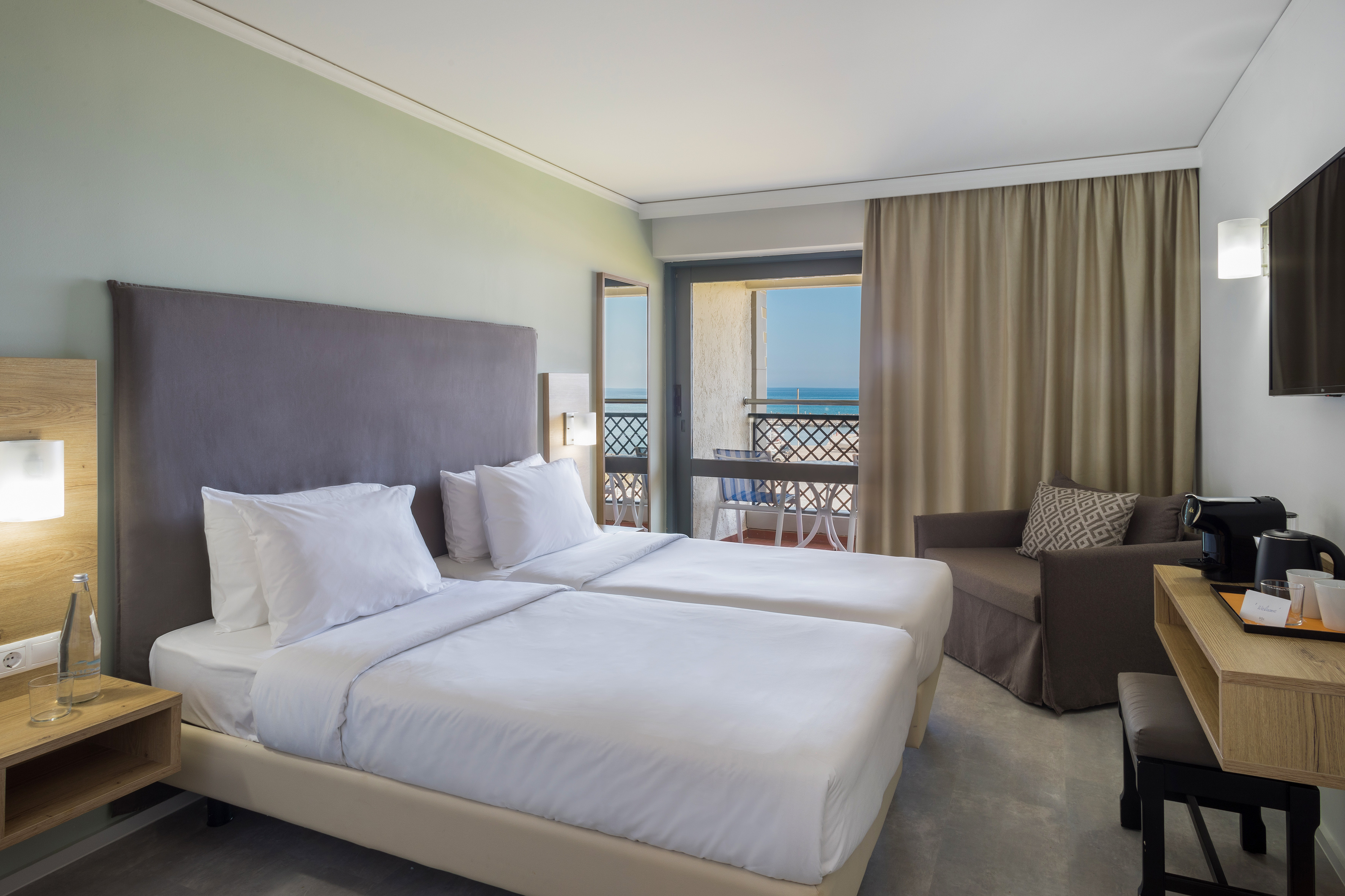 Modern resort room with twin beds, sea view balcony, and stylish decor.