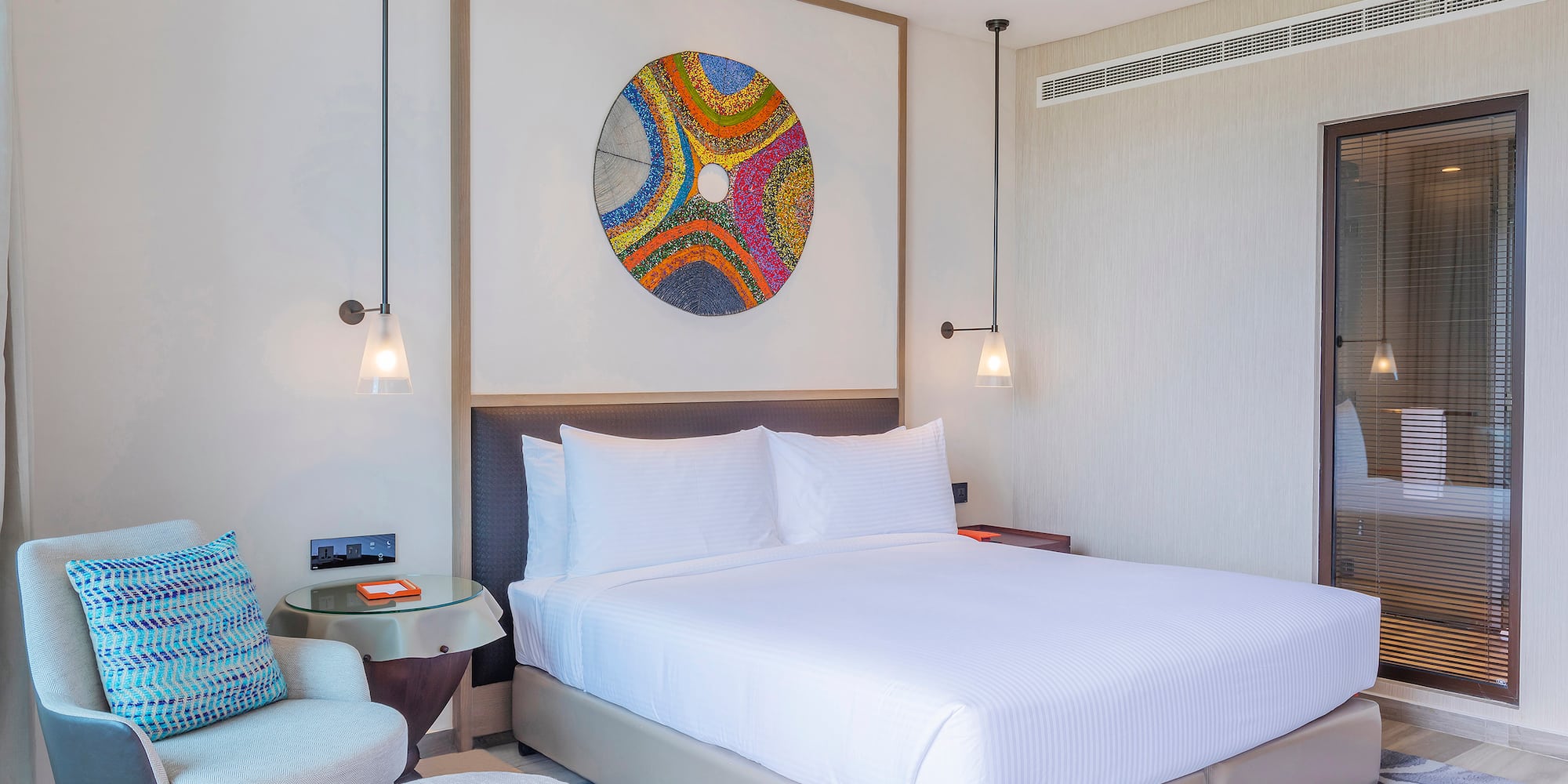 Stylish hotel bedroom with king bed, colorful abstract art, and modern furnishings.