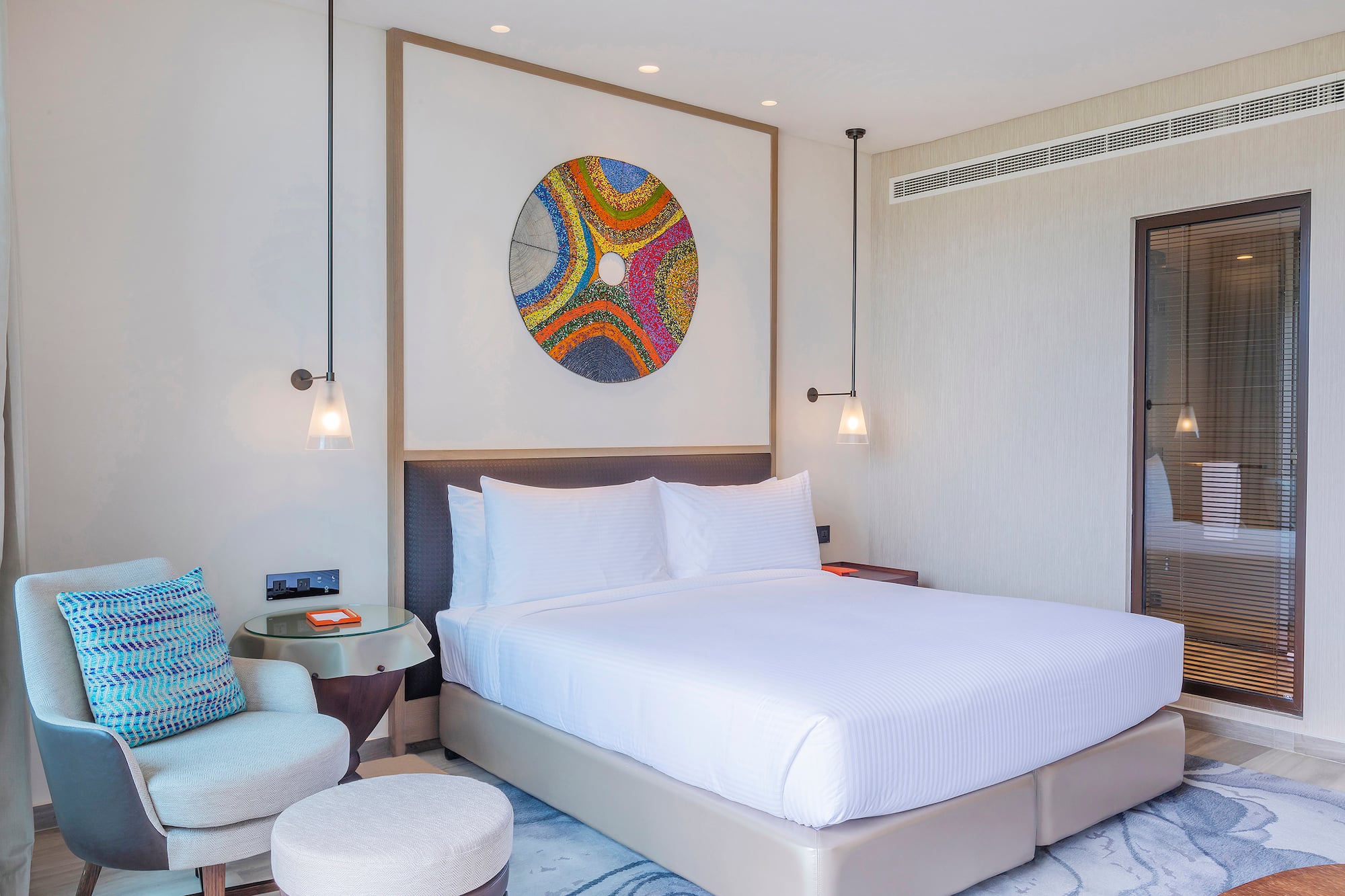 Stylish hotel bedroom with king bed, colorful abstract art, and modern furnishings.