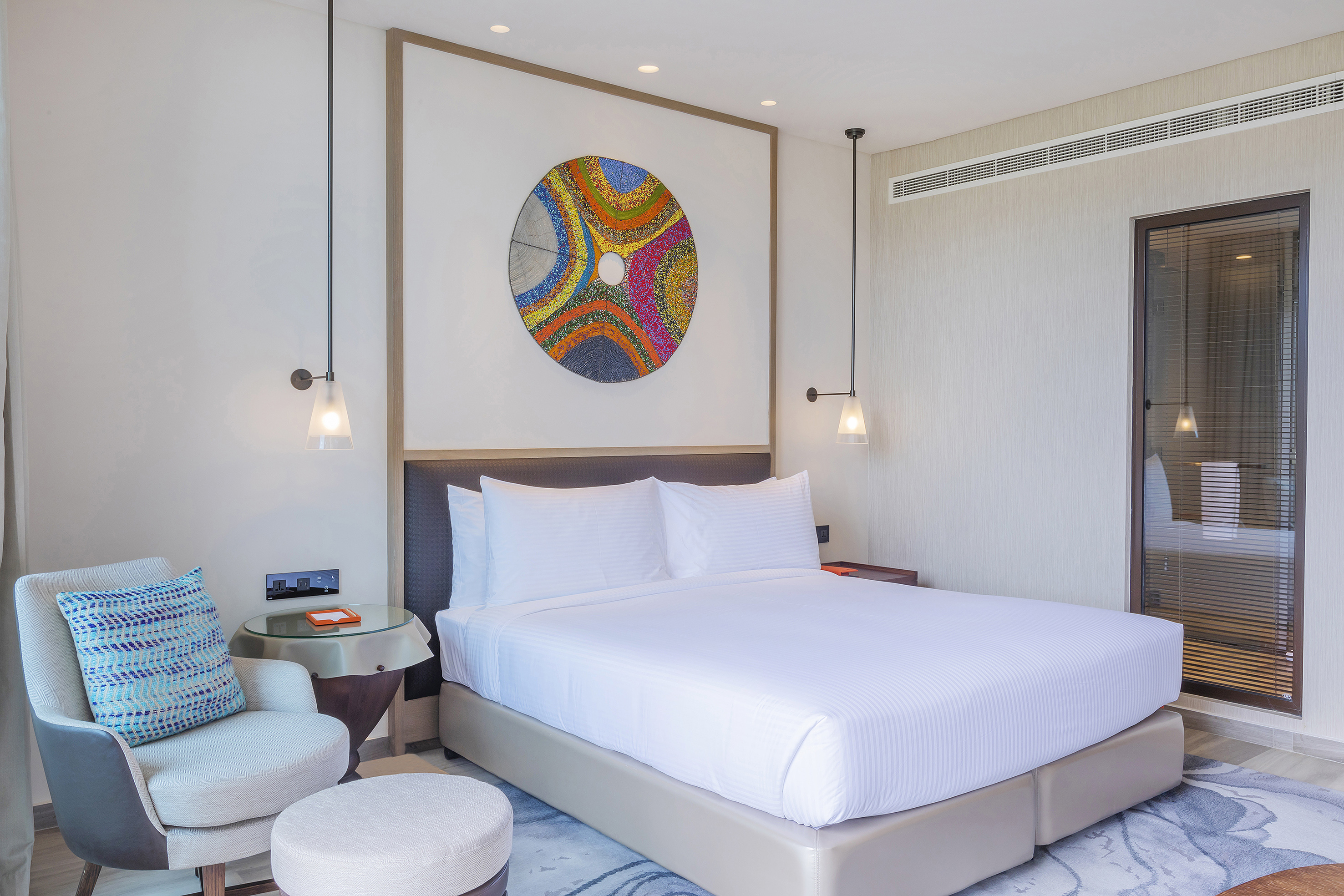 Stylish hotel bedroom with king bed, colorful abstract art, and modern furnishings.
