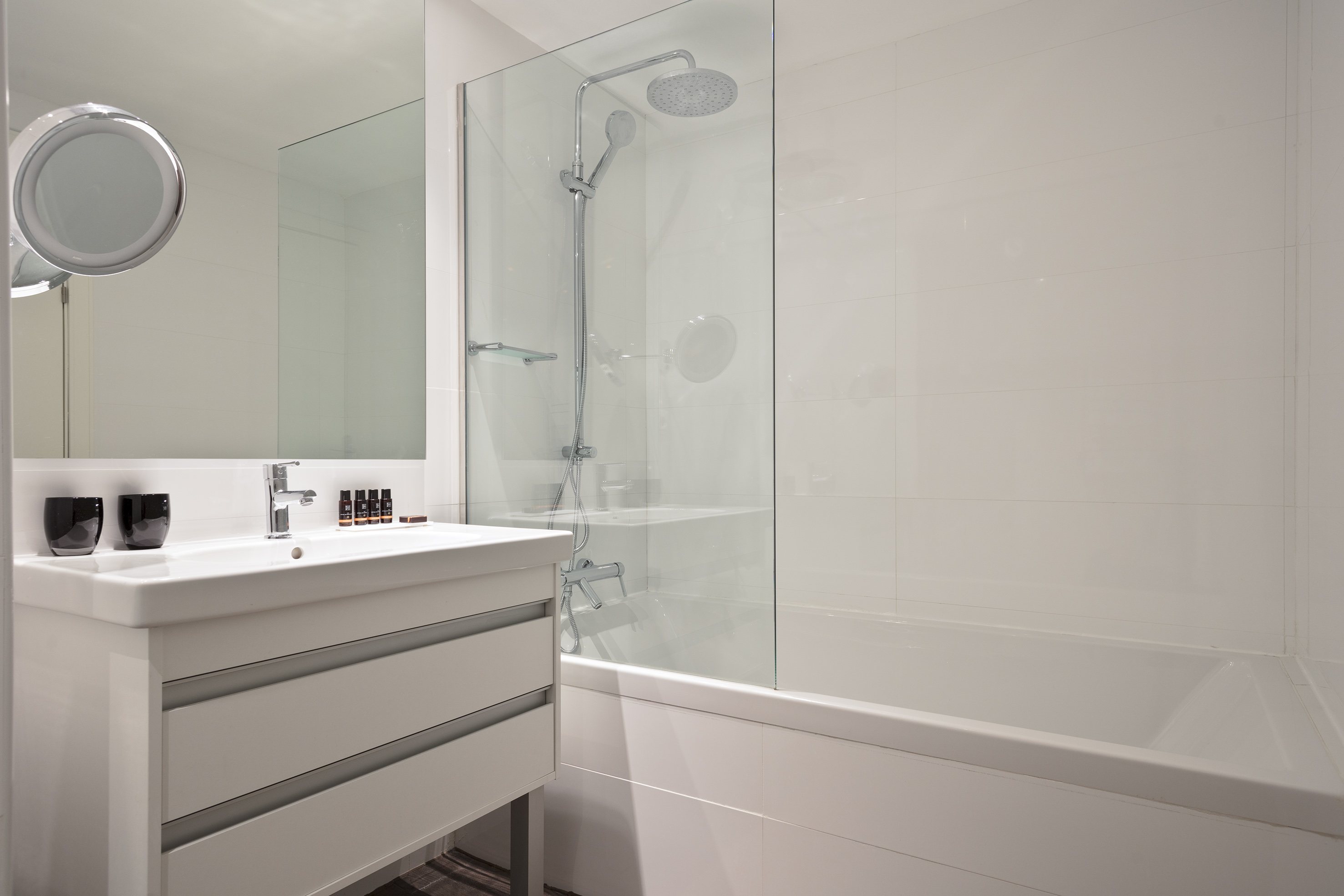 Modern white bathroom with vanity, sink, mirror, bathtub, and glass shower.