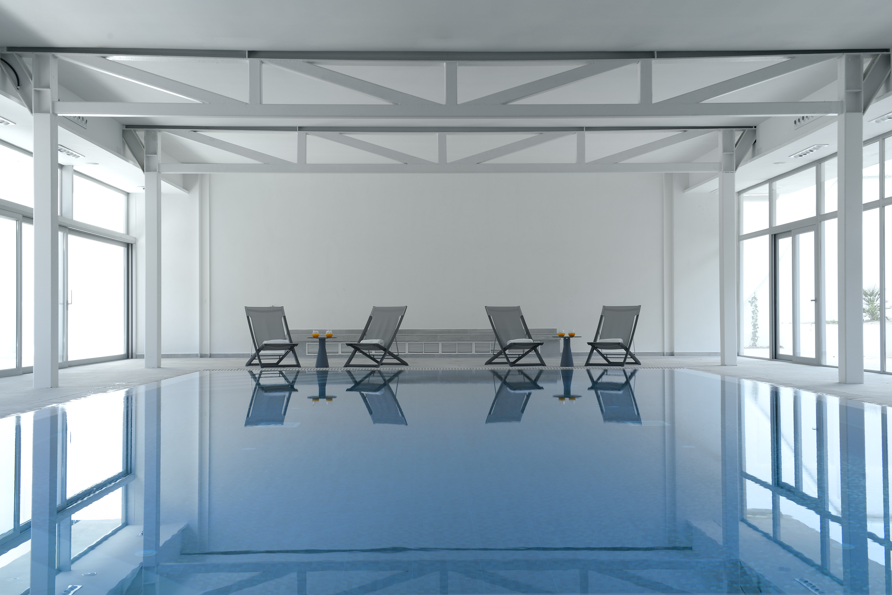 Modern indoor swimming pool with lounge chairs and bright windows.