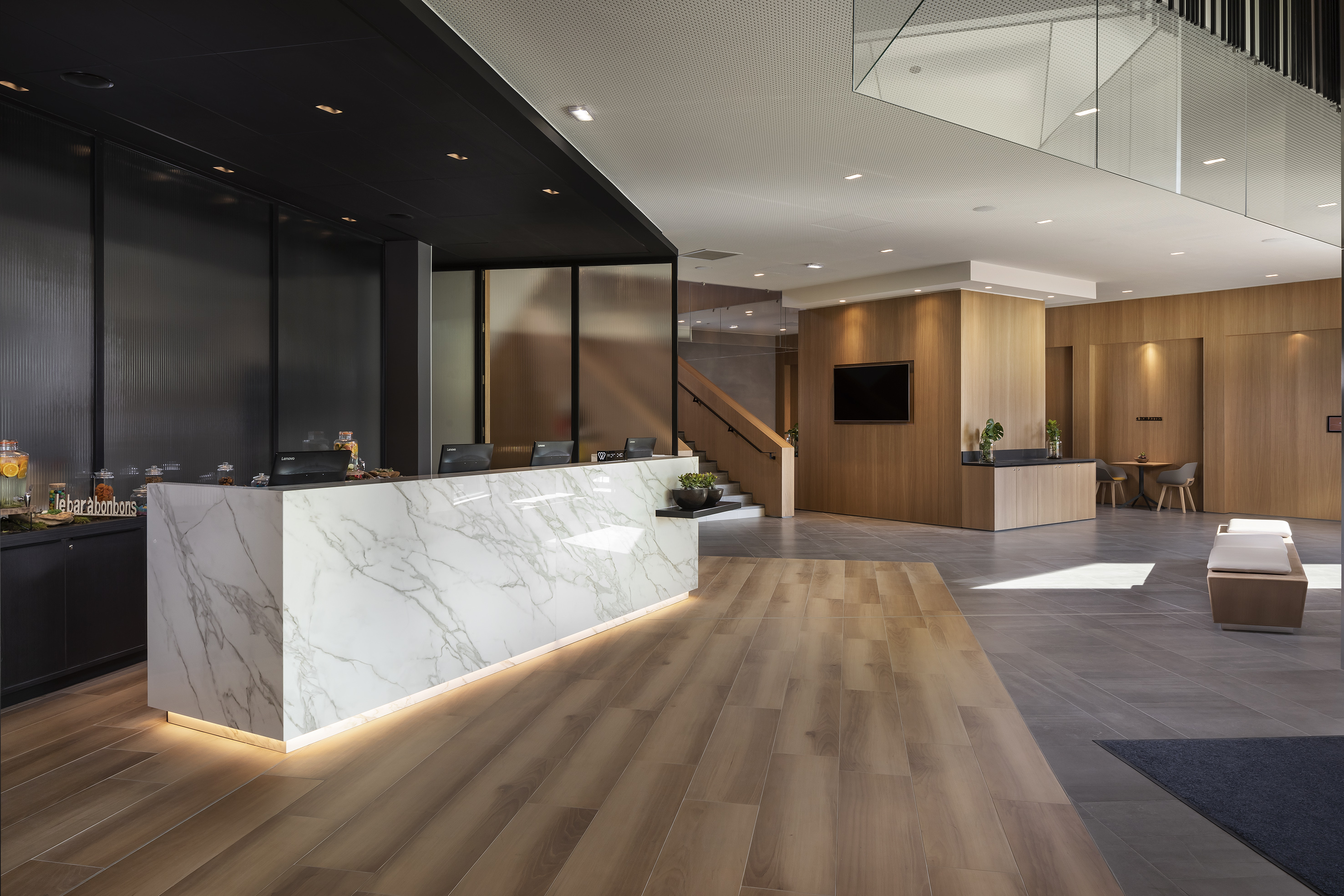 Modern hotel reception lobby with marble desk, wood accents, and staircase.