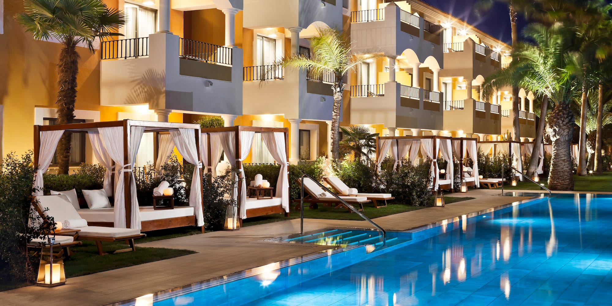 a pool with lounge chairs and a building with trees and lights