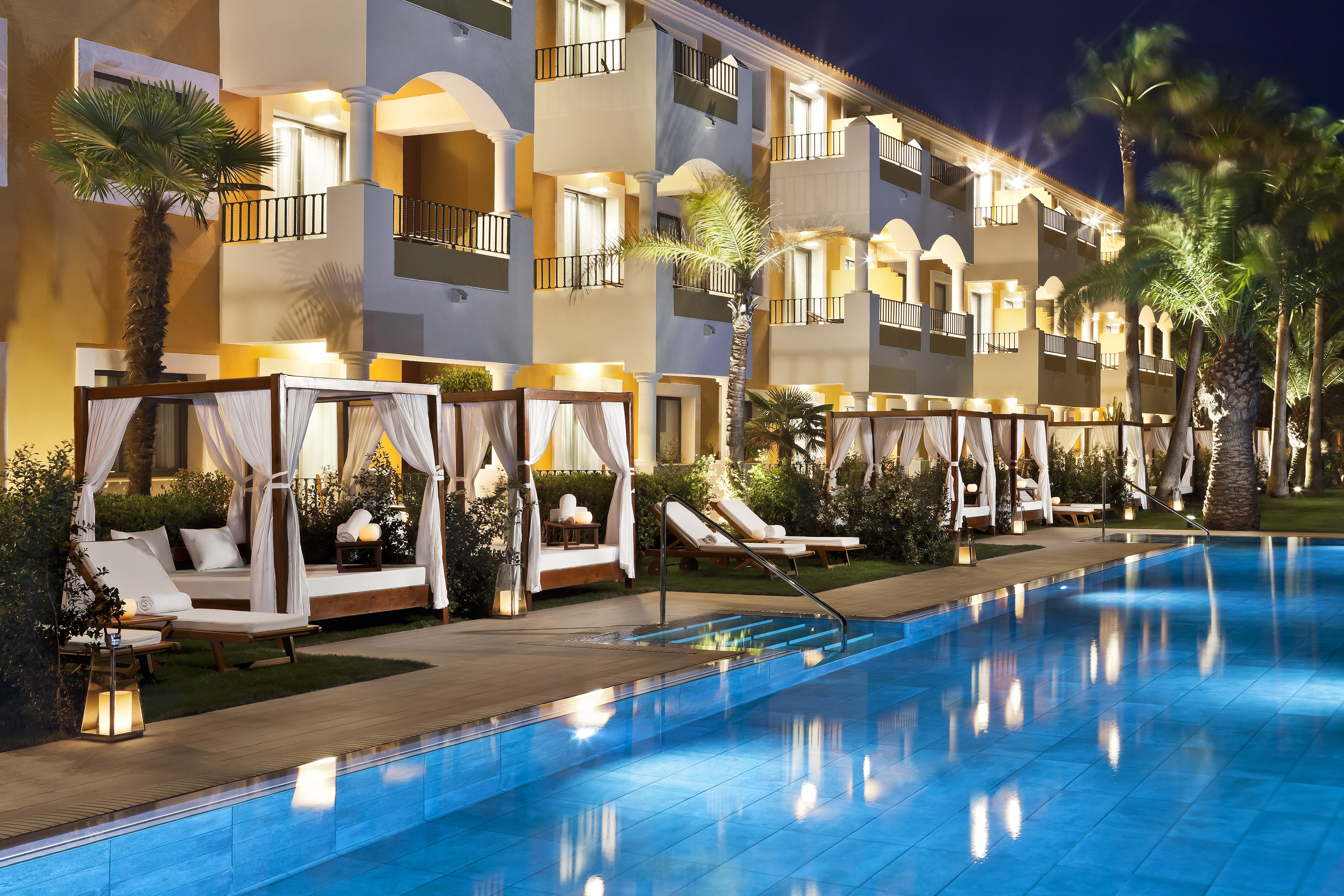a pool with lounge chairs and a building with trees and lights