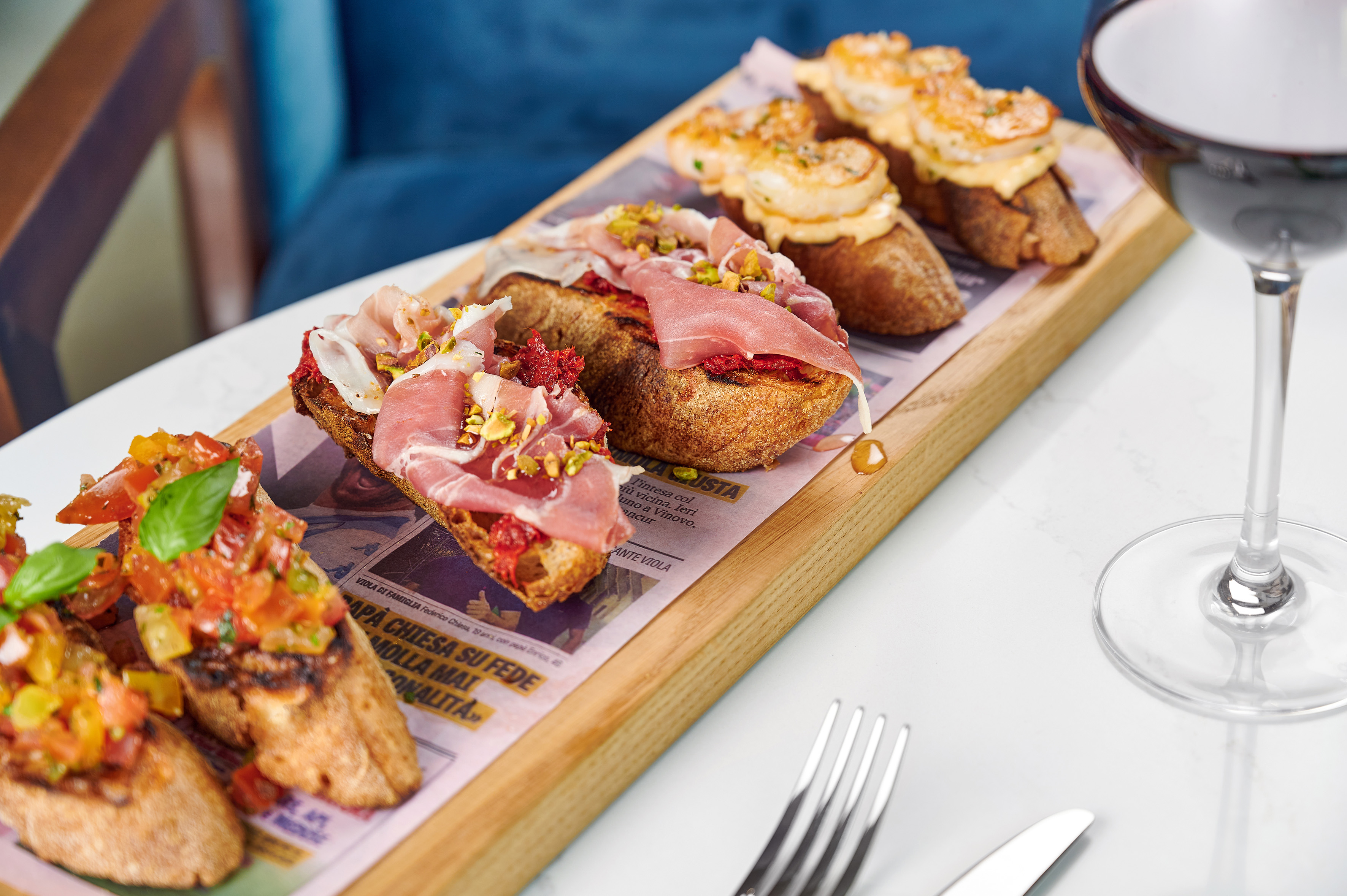 Assorted Italian bruschetta: tomato basil, prosciutto, shrimp. Red wine glass.