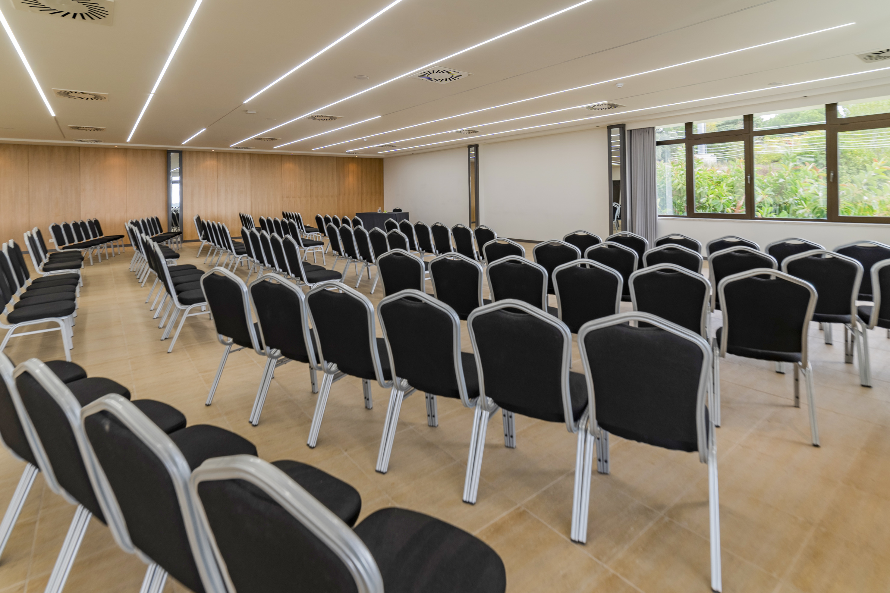 Empty conference room with rows of black chairs, large window, and modern lighting.