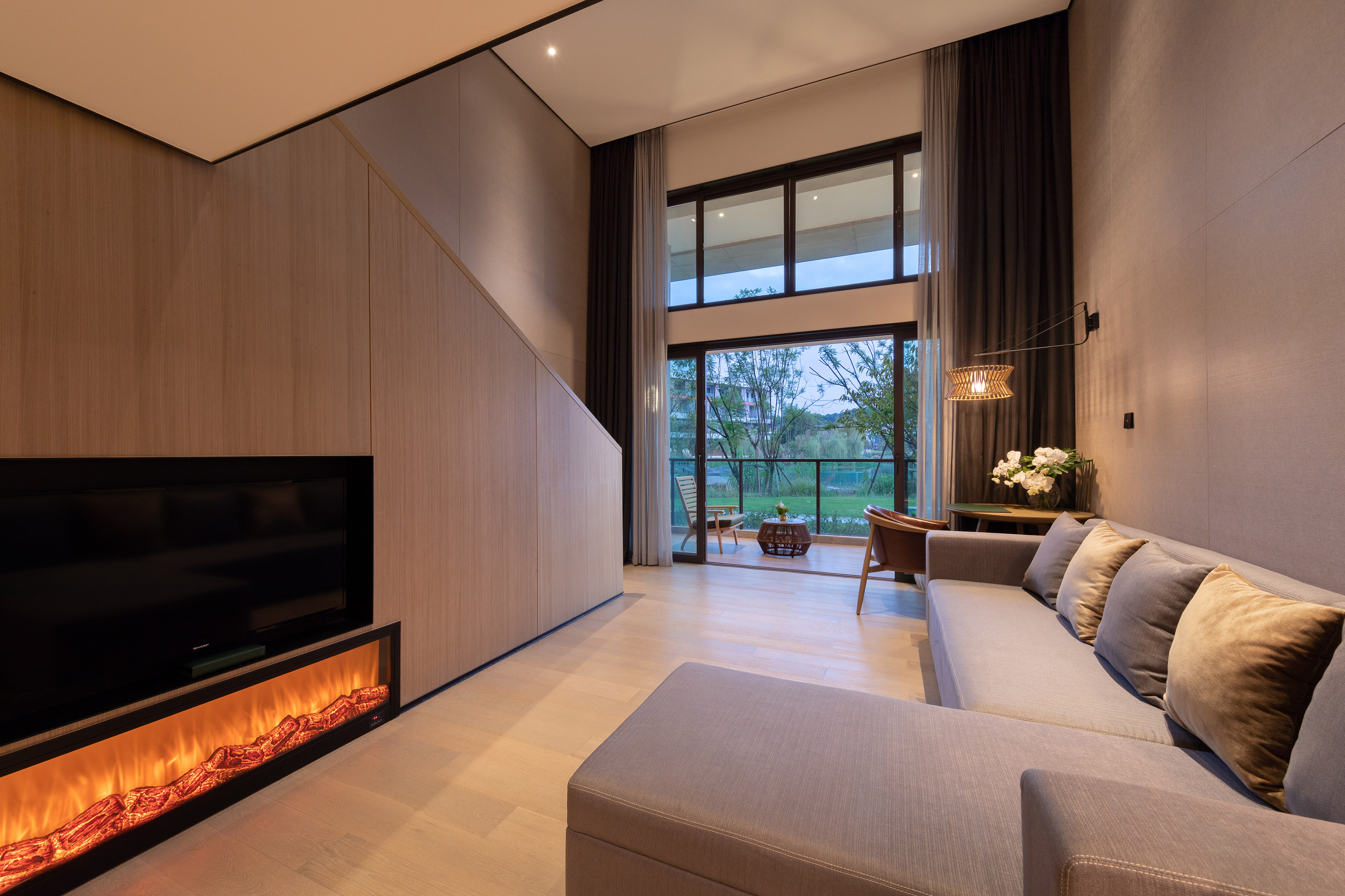 Modern living room: grey L-shaped sofa, electric fireplace, tall windows to patio.