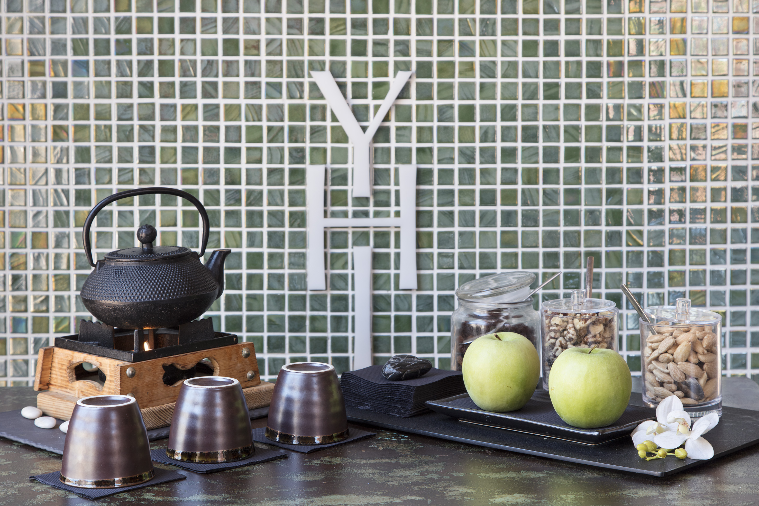 Cast iron tea set, green apples, nuts on counter, green mosaic wall, YH logo.