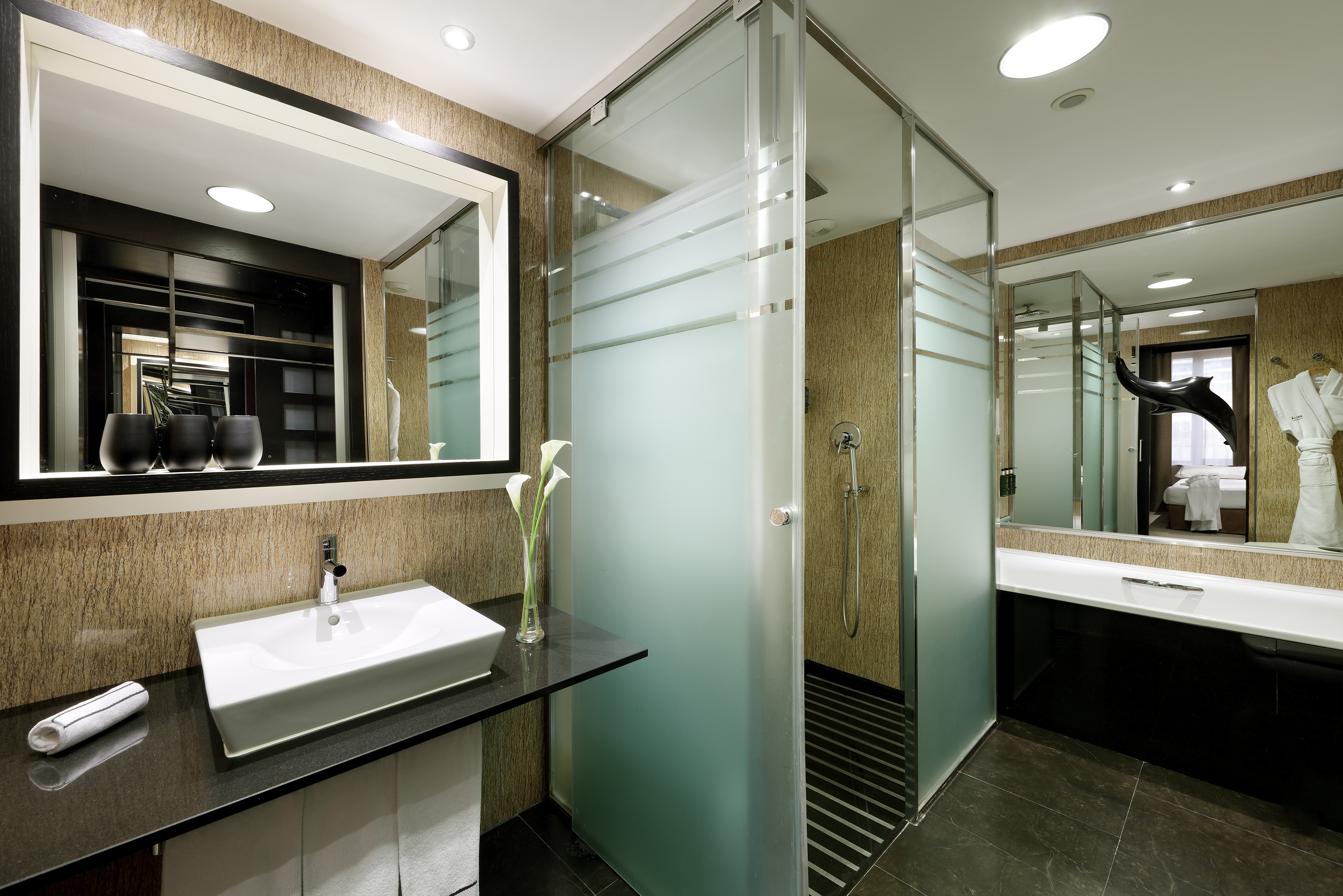 Sleek hotel bathroom with vessel sink, large mirror, and frosted glass shower.