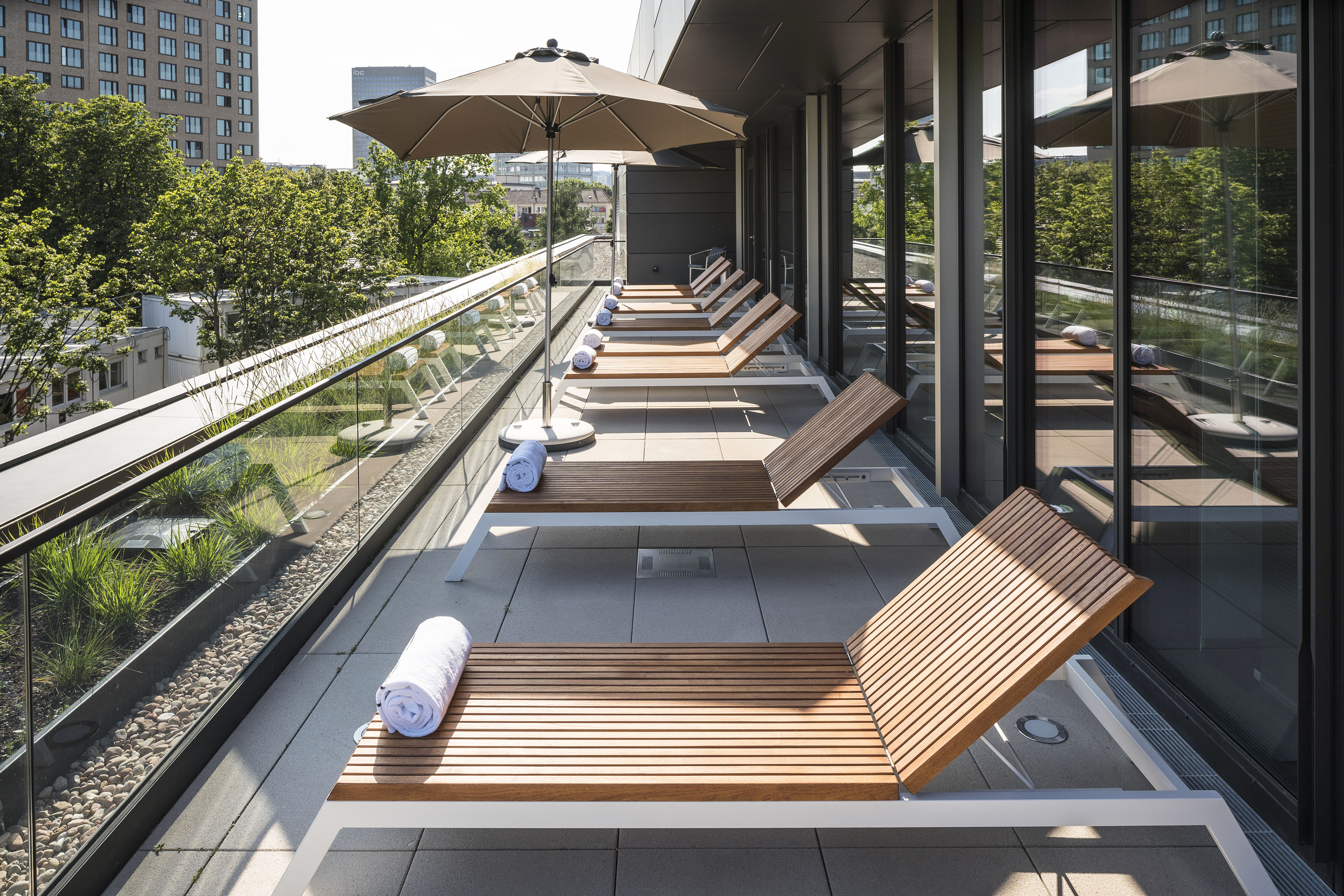 Rooftop terrace with modern sunbeds, umbrella, and urban cityscape views.