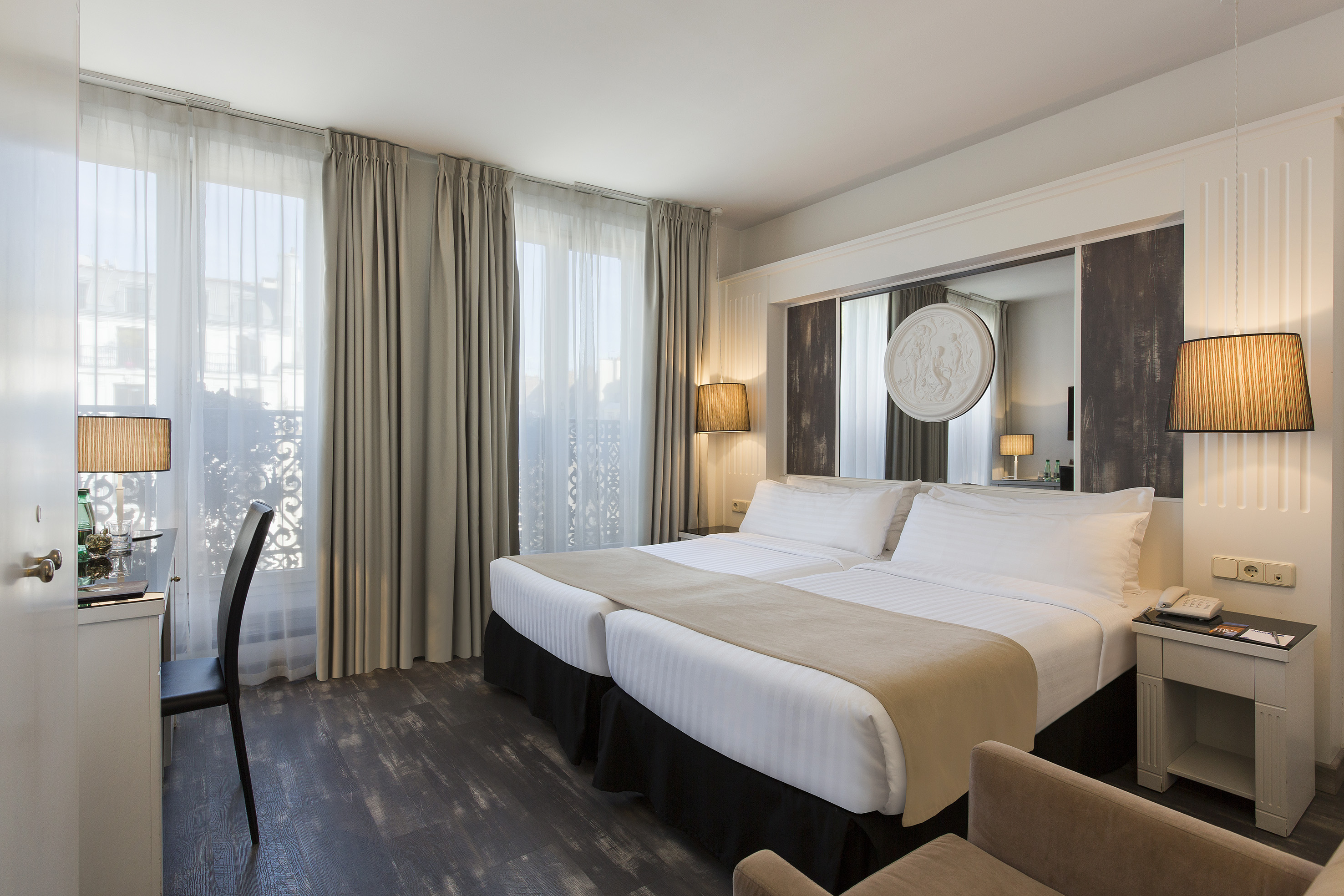 Elegant hotel room with twin beds, desk, and bright windows.