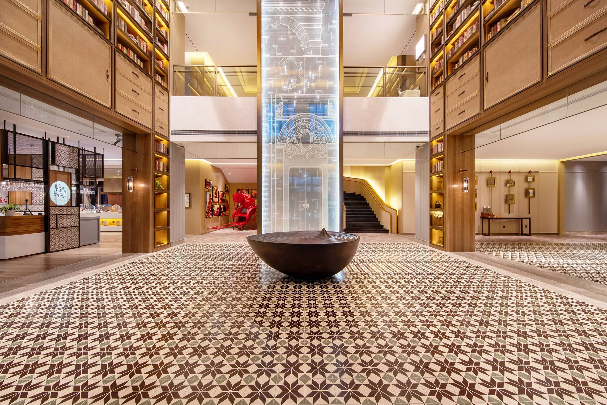 Grand hotel lobby with geometric floor, central water feature, and library bookshelves.