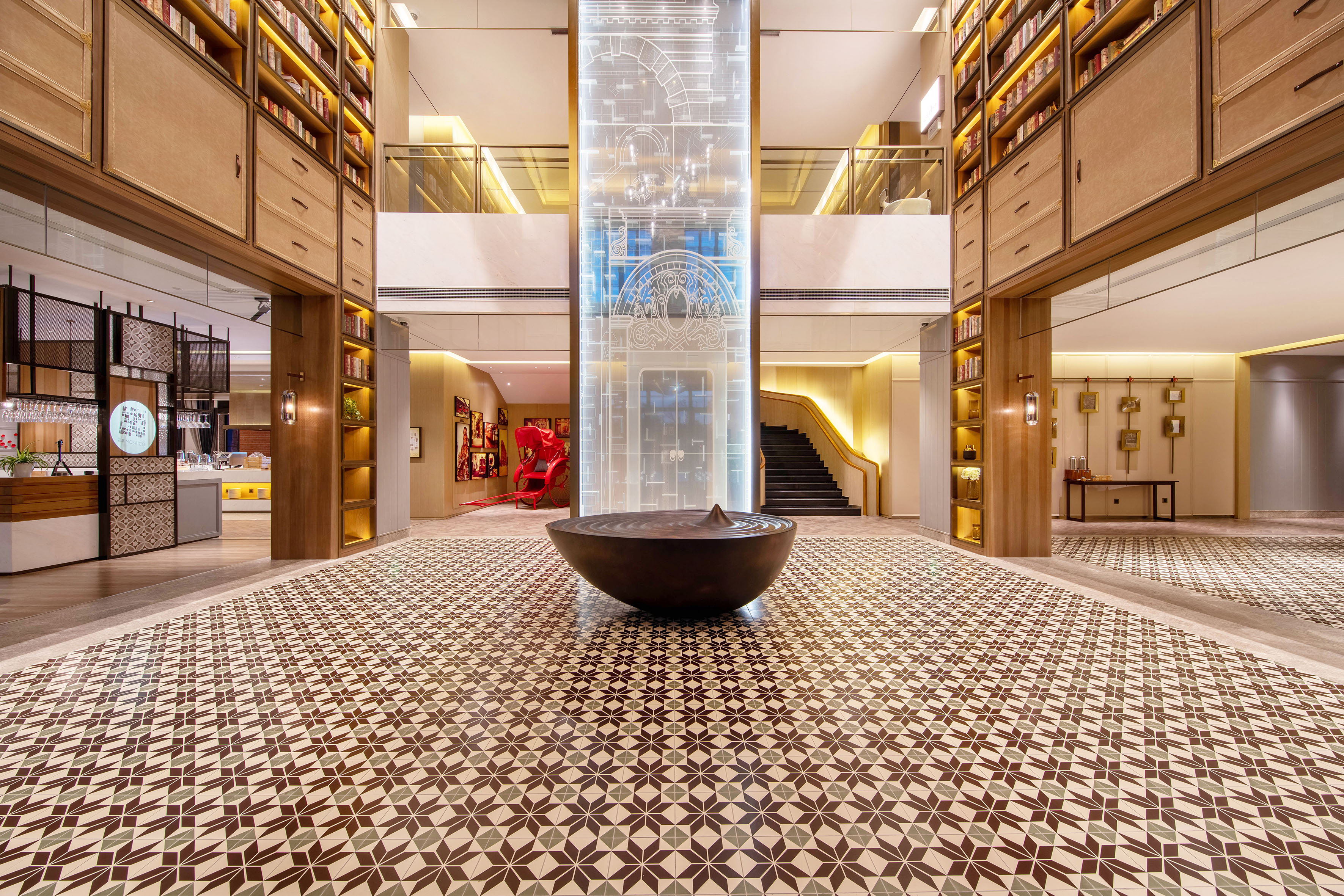 Grand hotel lobby with geometric floor, central water feature, and library bookshelves.