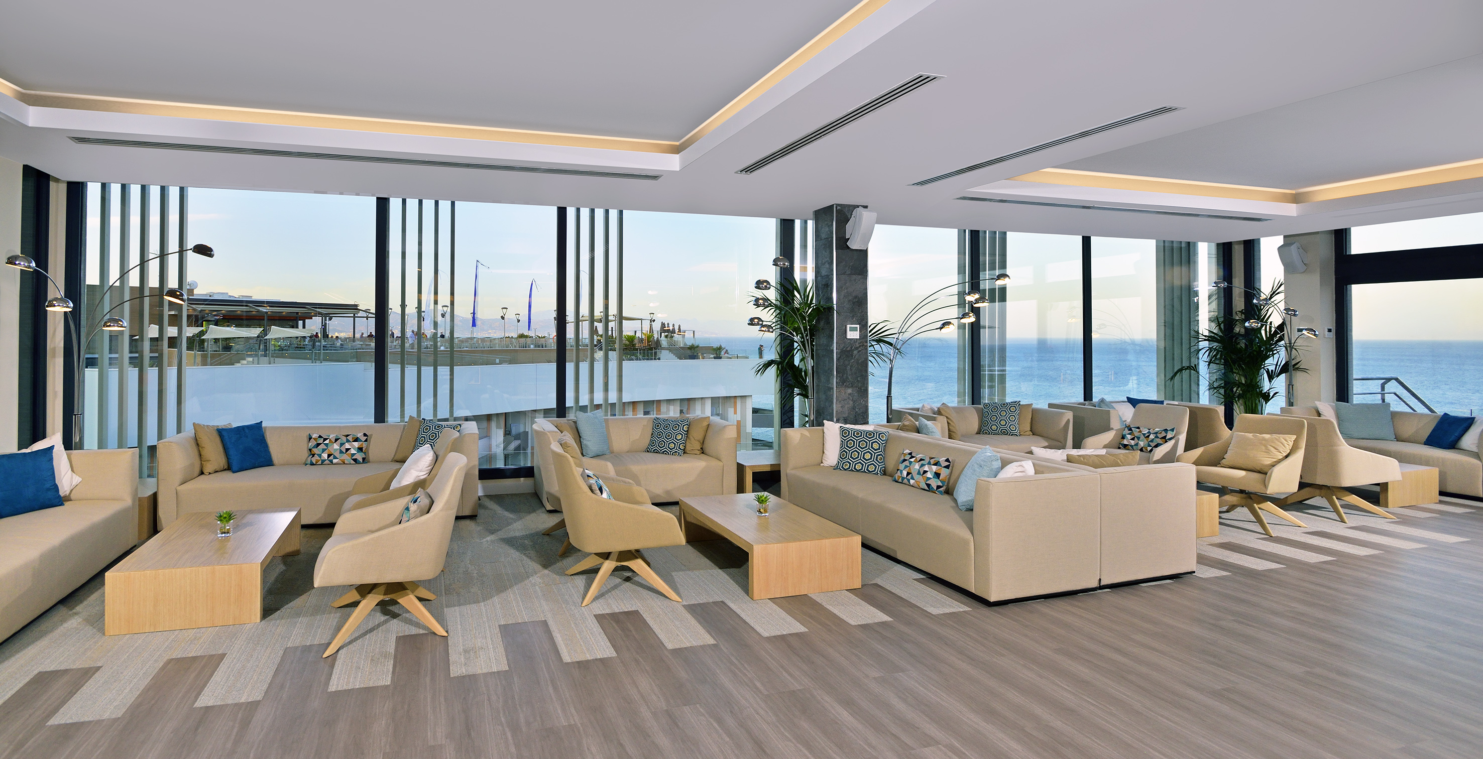 Modern hotel lounge with ocean view, beige sofas, and large windows.